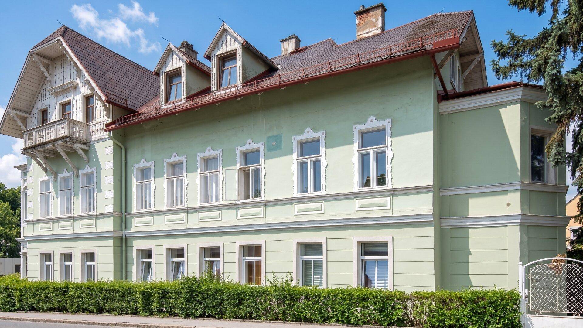 Seitenansicht des historischen Gebäudes mit vielen Fenstern und einem gepflegten Vorgarten.