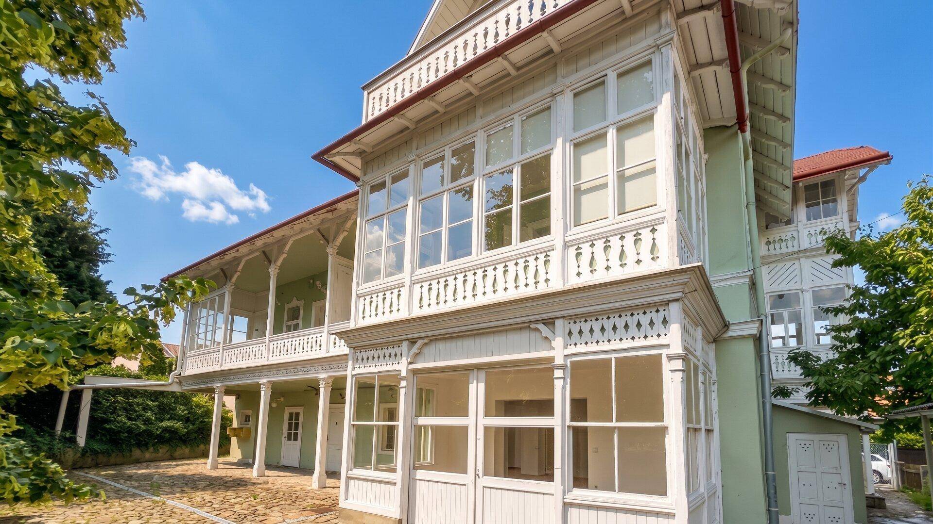 Eingangsbereich des historischen Gebäudes mit verglaster Veranda und kunstvollen Holzdetails.