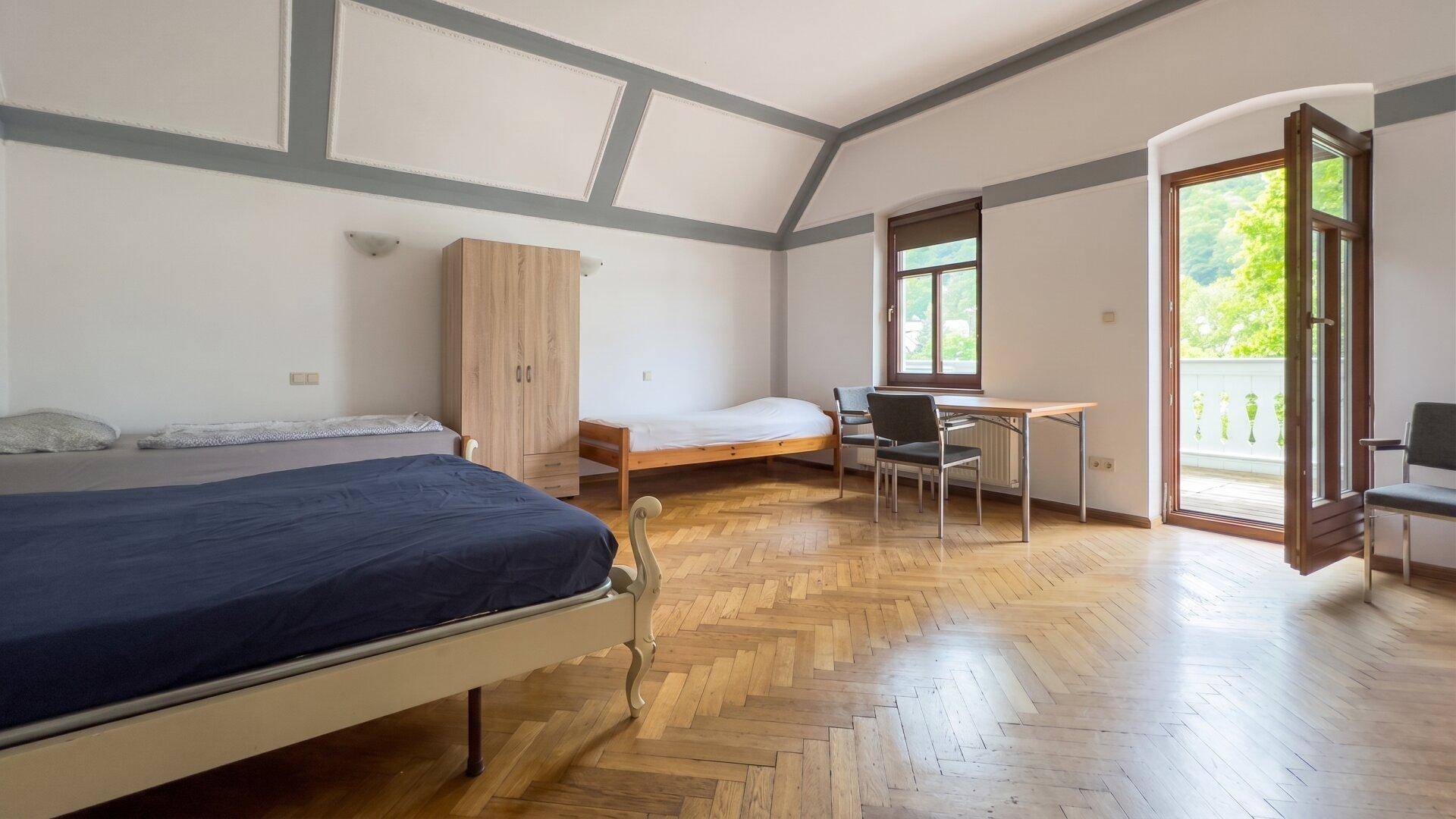 Geräumiges Schlafzimmer mit Fischgrätparkett, hohen Decken und direktem Zugang zum Balkon.