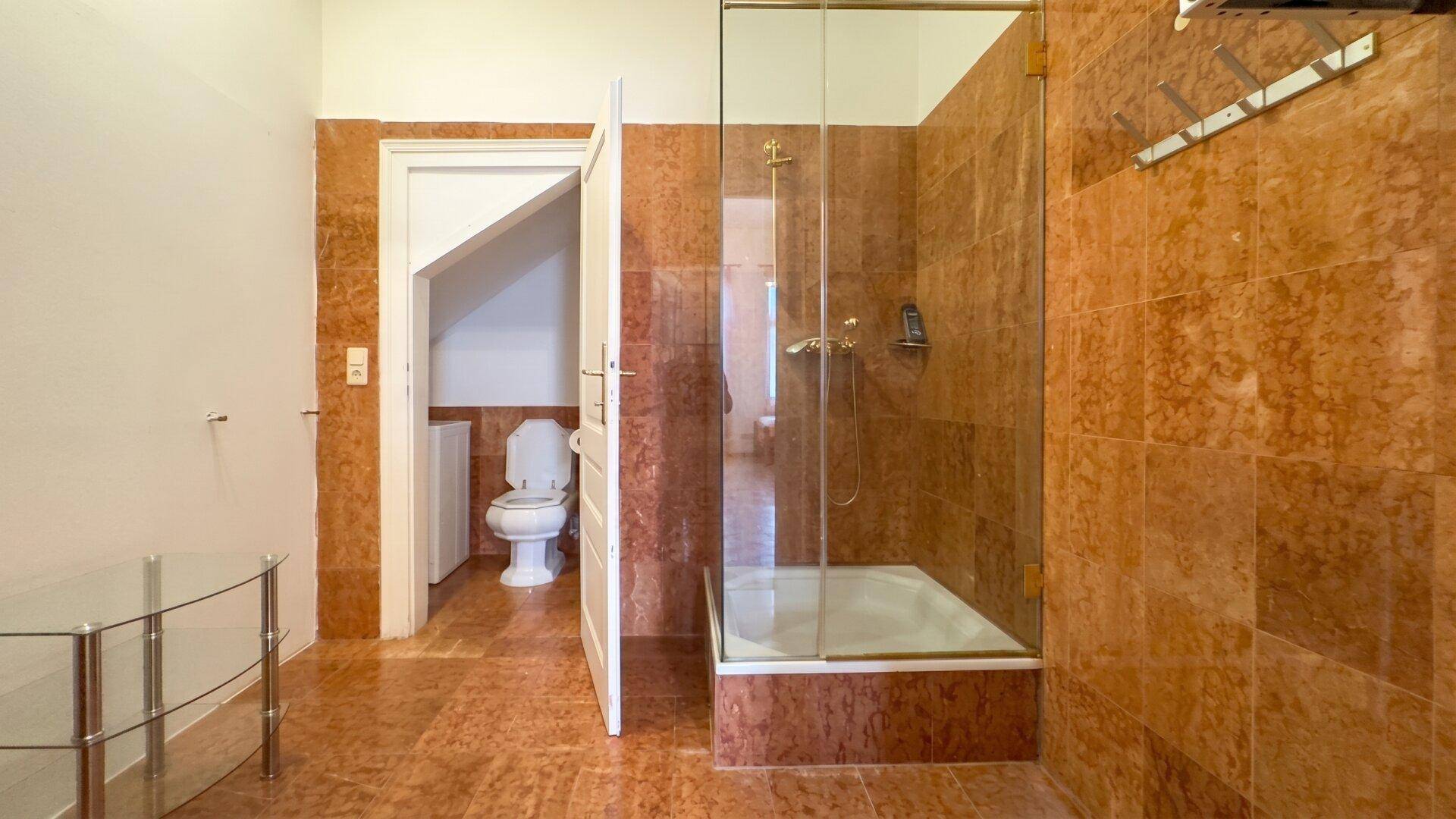 Badezimmer mit braunen Fliesen, Duschkabine und separatem WC-Bereich unter der Dachschräge.