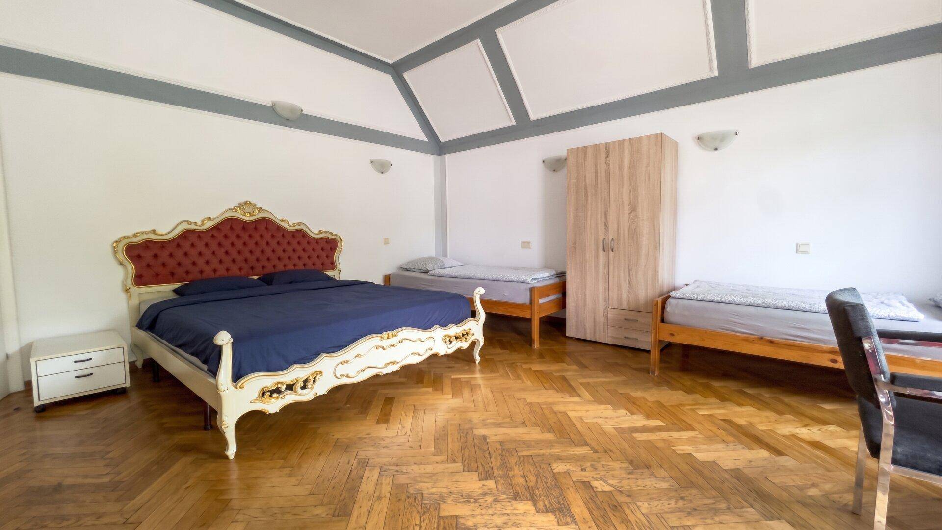 Helles Schlafzimmer mit mehreren Betten, Holzboden und dekorativer Deckenverkleidung.