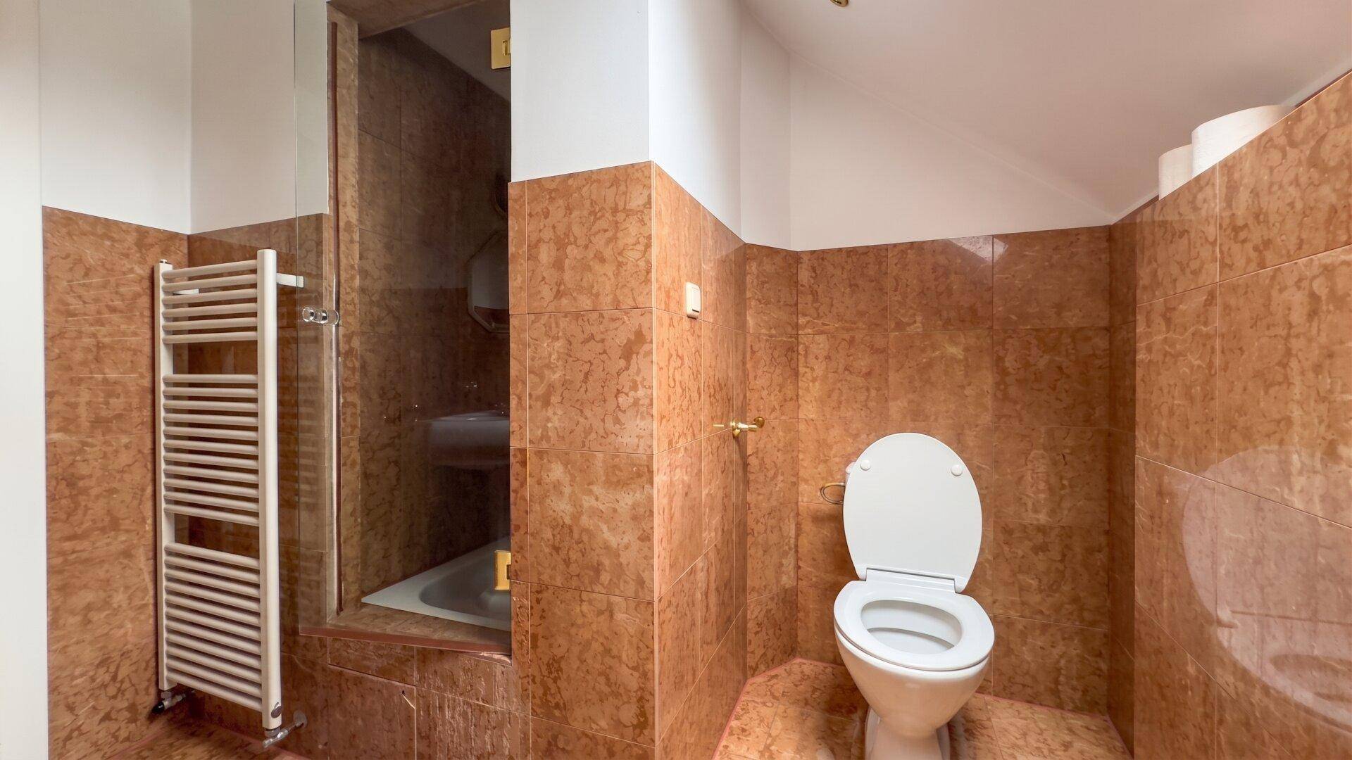 Gefliestes Badezimmer mit Toilette, Duschkabine und beheiztem Handtuchhalter.