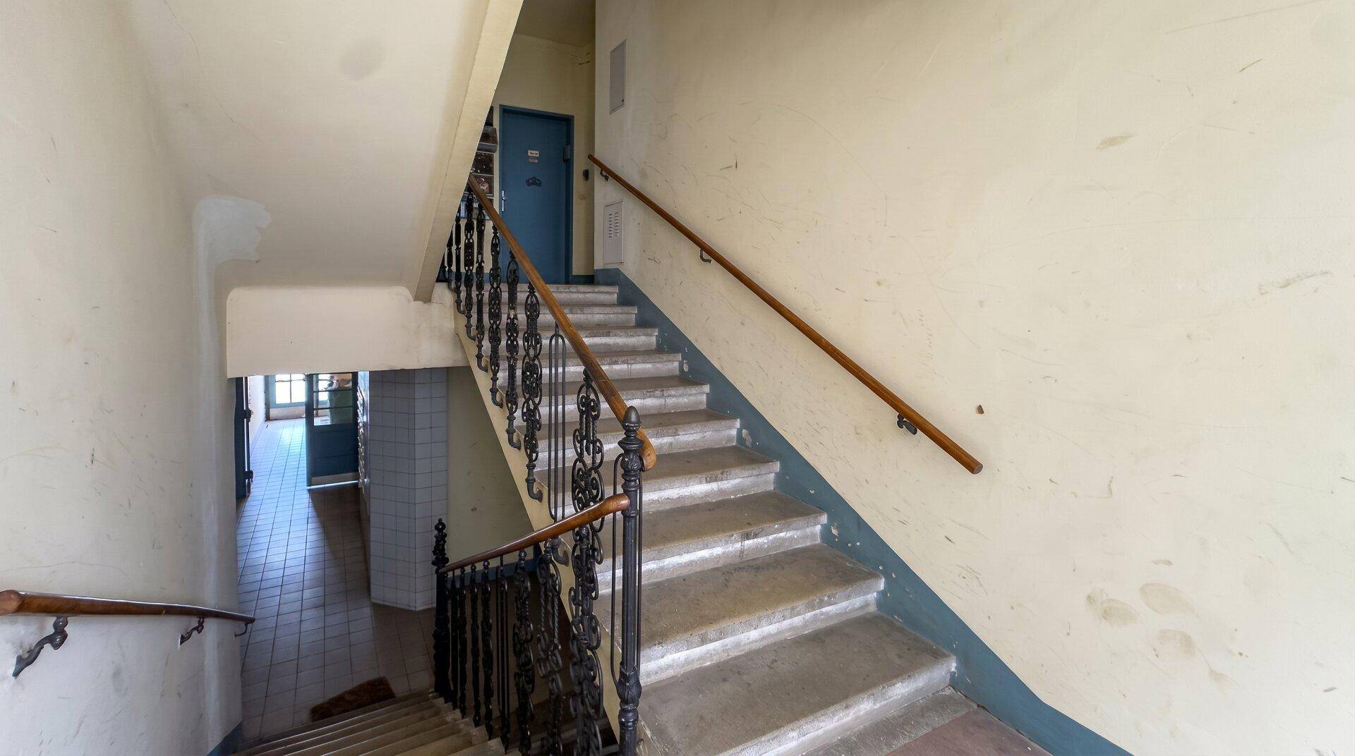 Altes Treppenhaus mit schmiedeeisernem Geländer und Holzhandlauf in einem Mehrfamilienhaus.