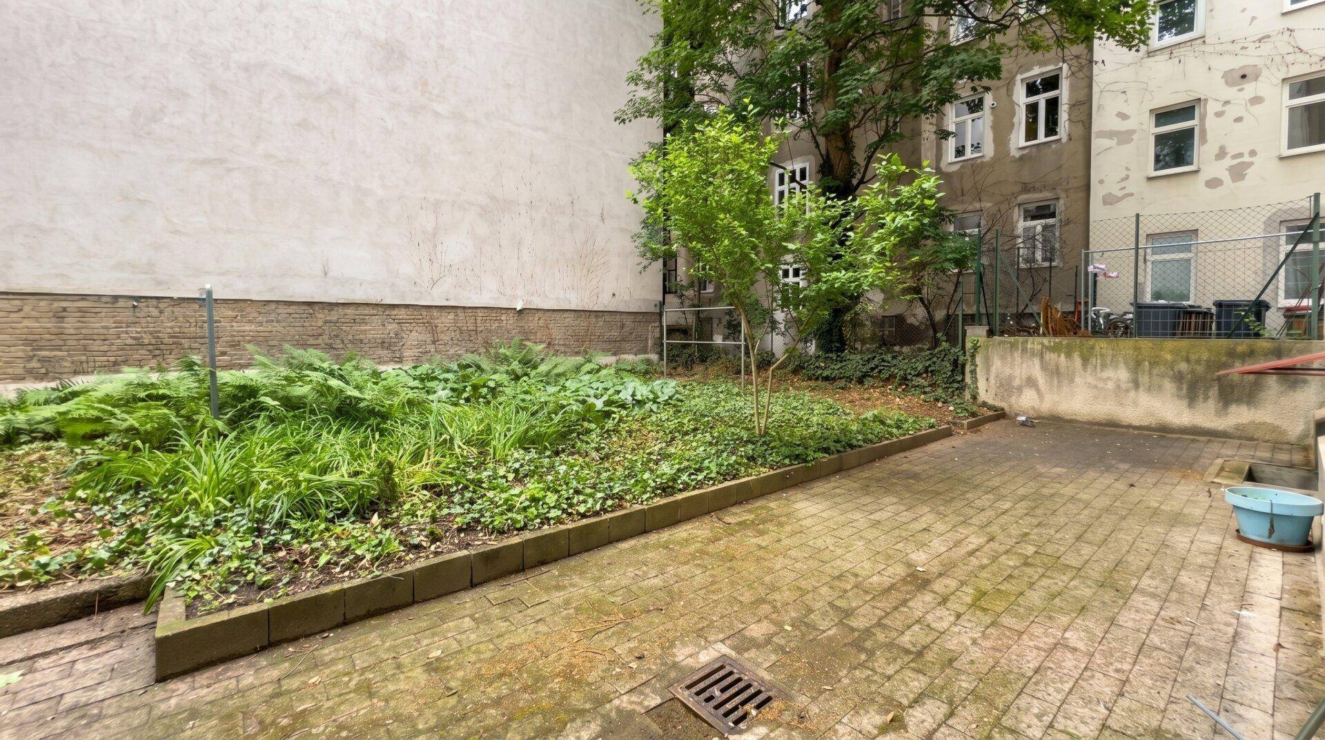 Gepflasterter Innenhof mit Hochbeet und umgebenden Altbauten, bietet Potenzial für eine grüne Oase.