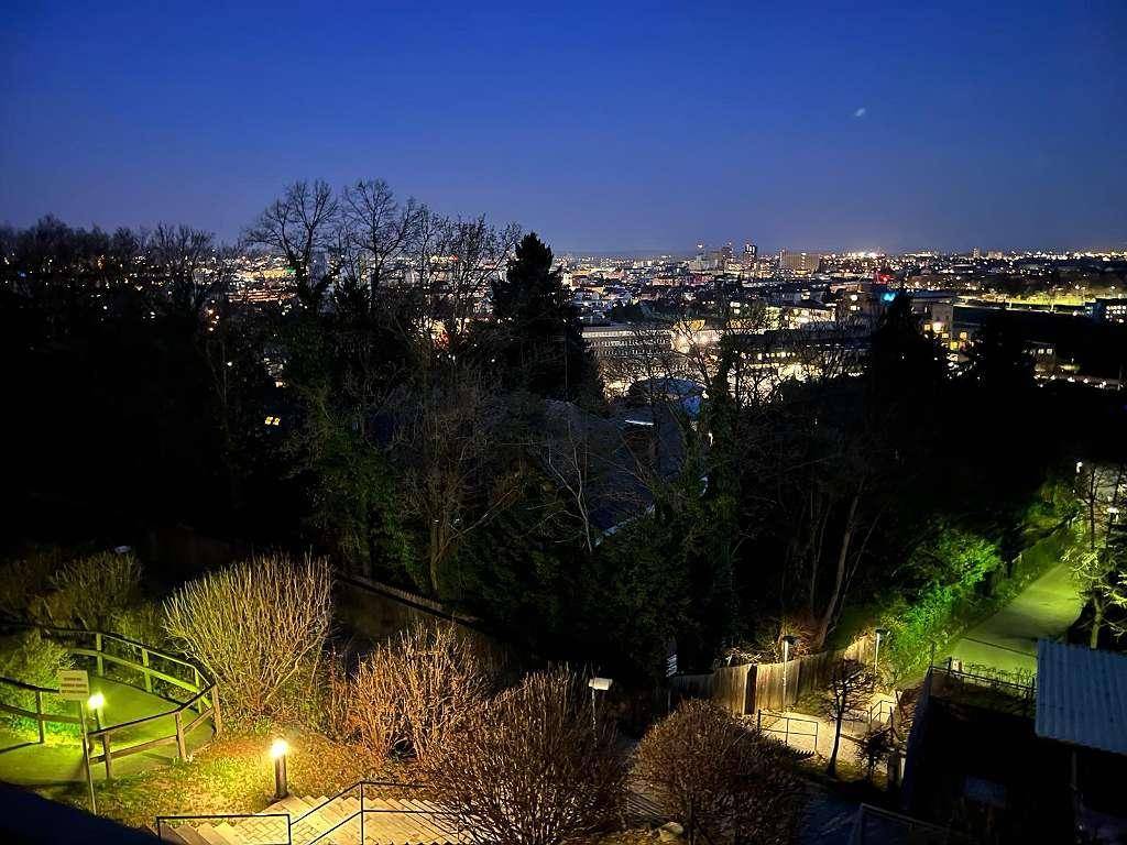 Nächtlicher Panoramablick auf die beleuchtete Stadt und die umliegende grüne Landschaft.