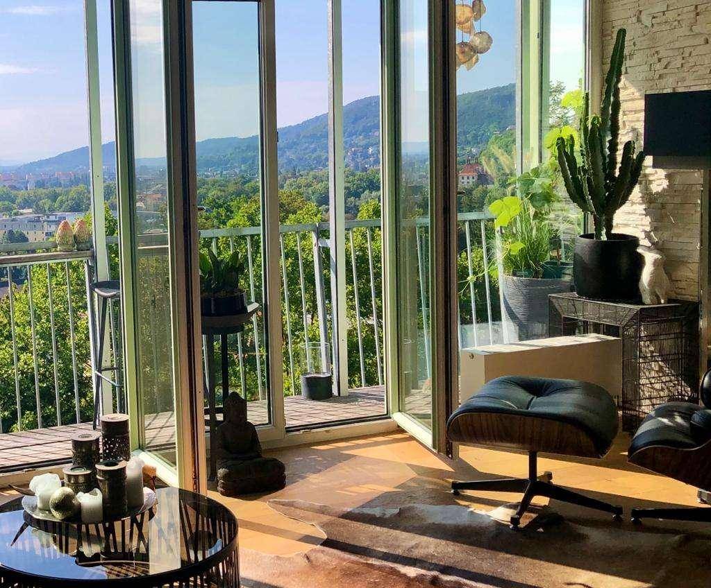 Helles Wohnzimmer mit raumhohen Fenstern und beeindruckendem Blick auf Berge und die Stadt.