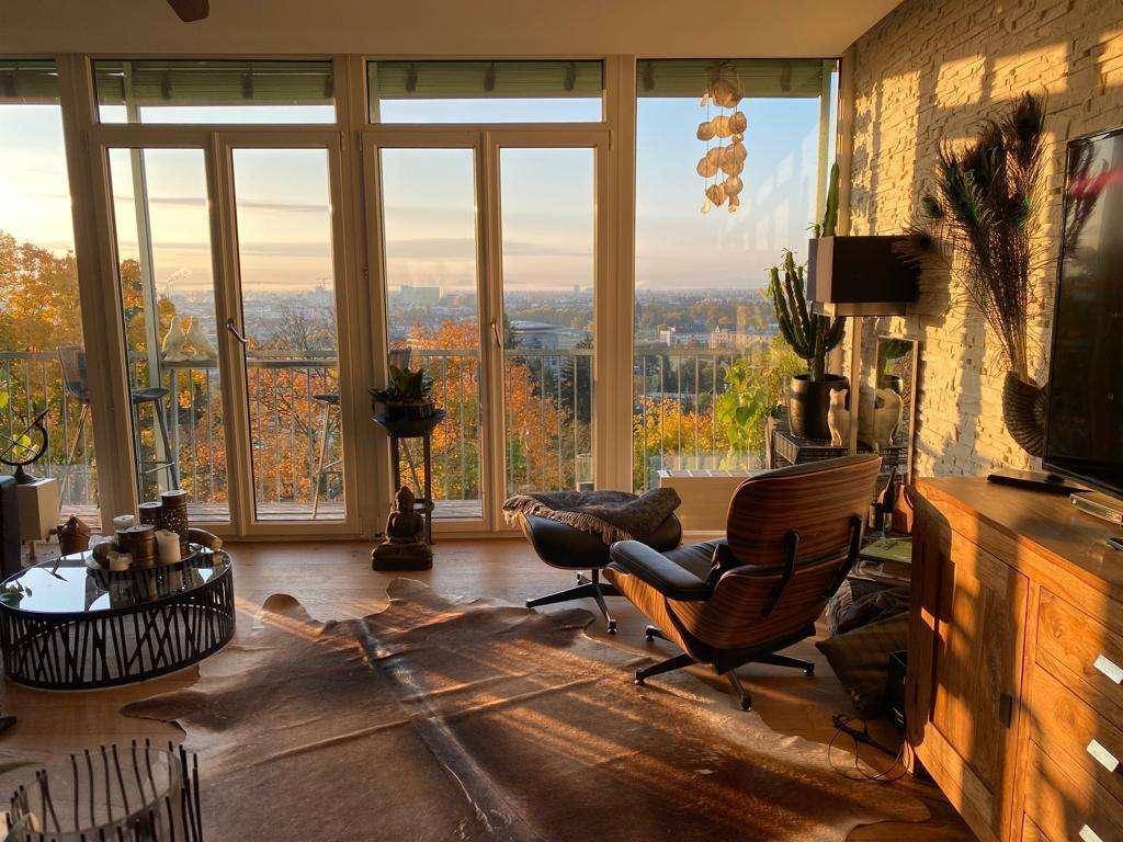 Lichtdurchflutetes Wohnzimmer mit Panoramafenstern und weitem Blick über die herbstliche Stadtlandschaft.