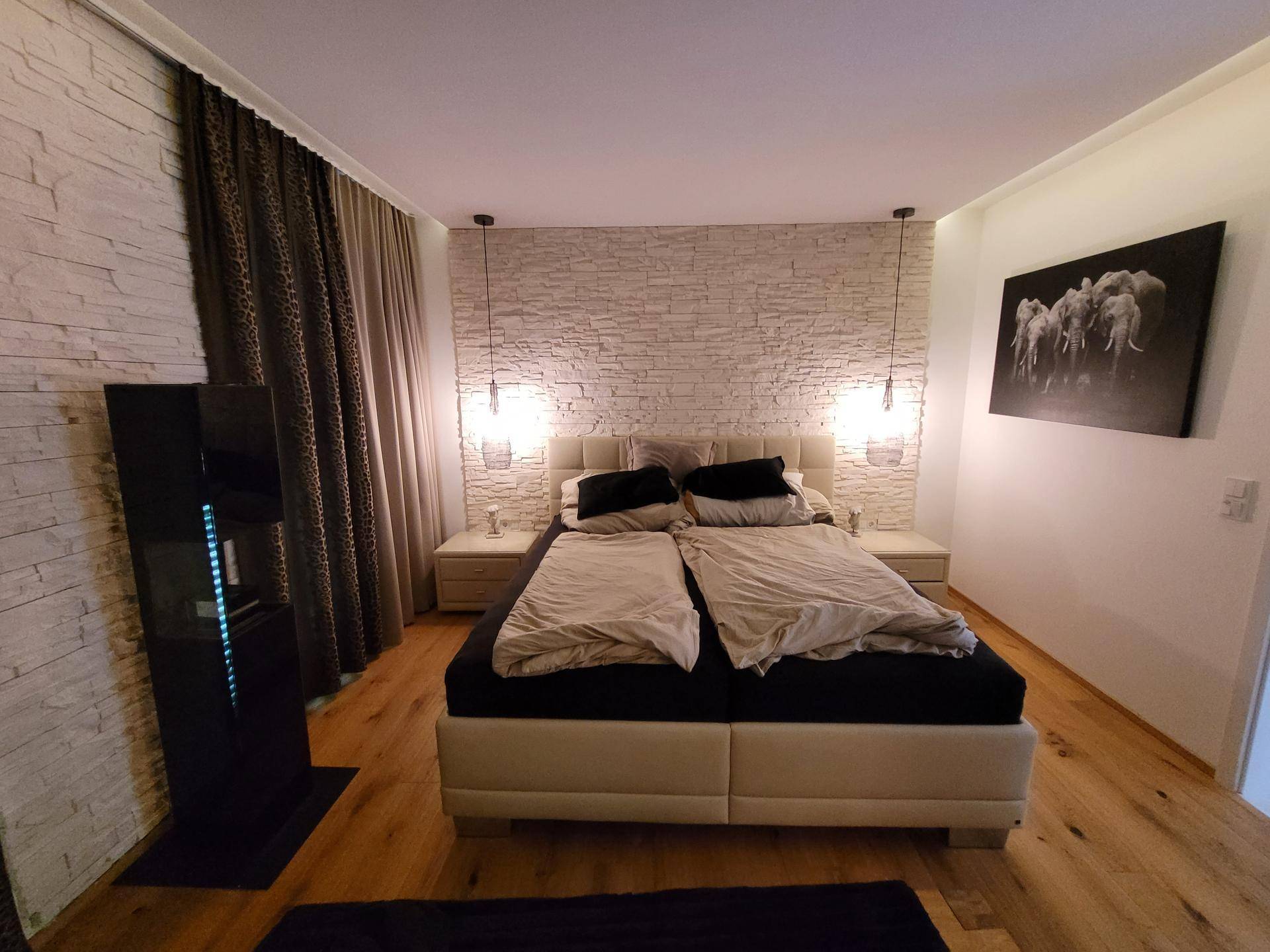 Modernes Schlafzimmer mit bequemen Bett, dekorativer Steinwand und warmem Holzfußboden.
