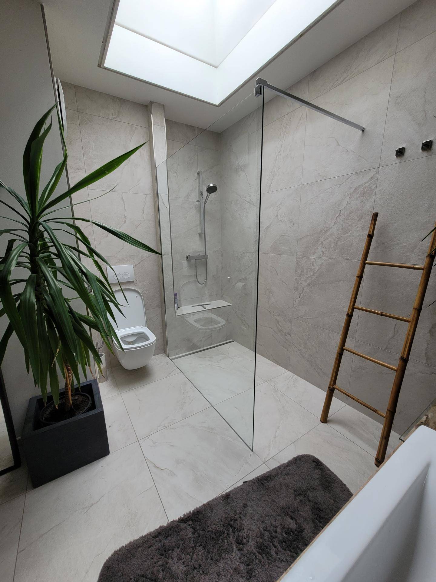 Modernes Badezimmer mit begehbarer Dusche, Wand-WC und einem Oberlicht für natürliches Licht.