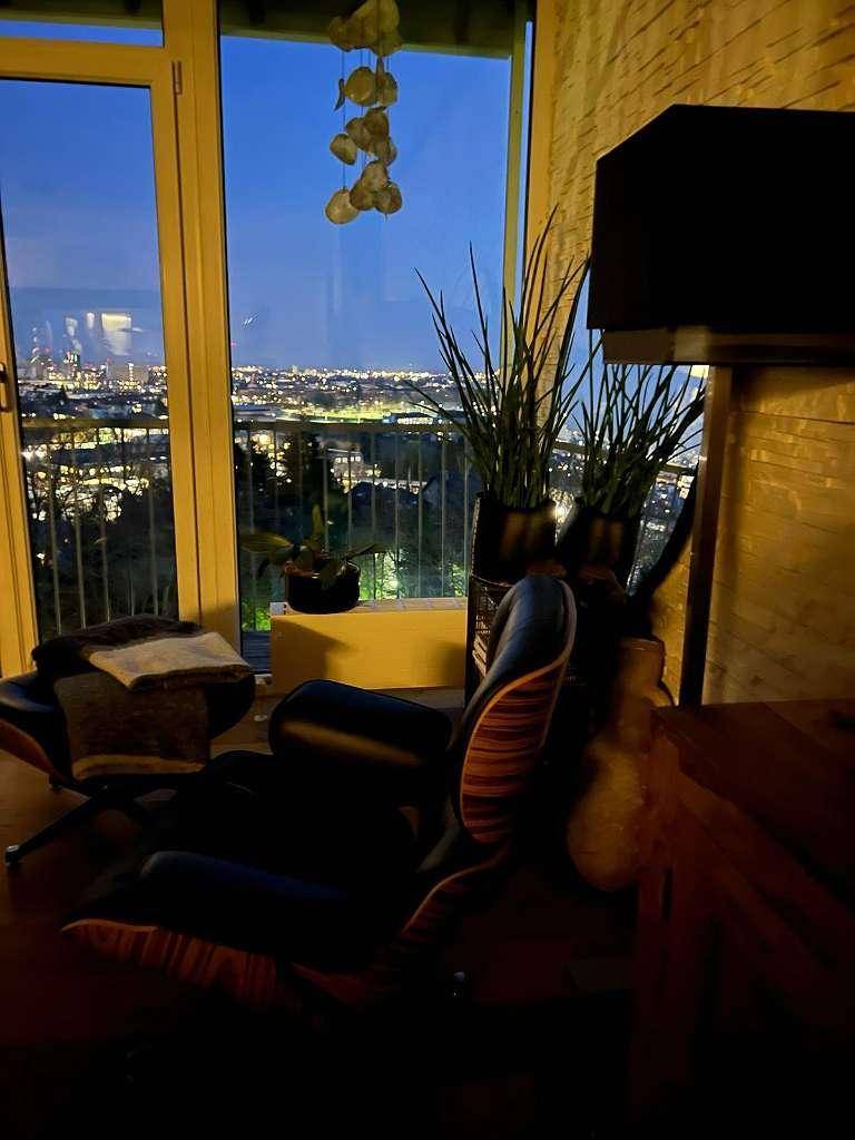 Gemütlicher Sessel am Fenster mit nächtlichem Blick auf die beleuchtete Stadt und die Umgebung.