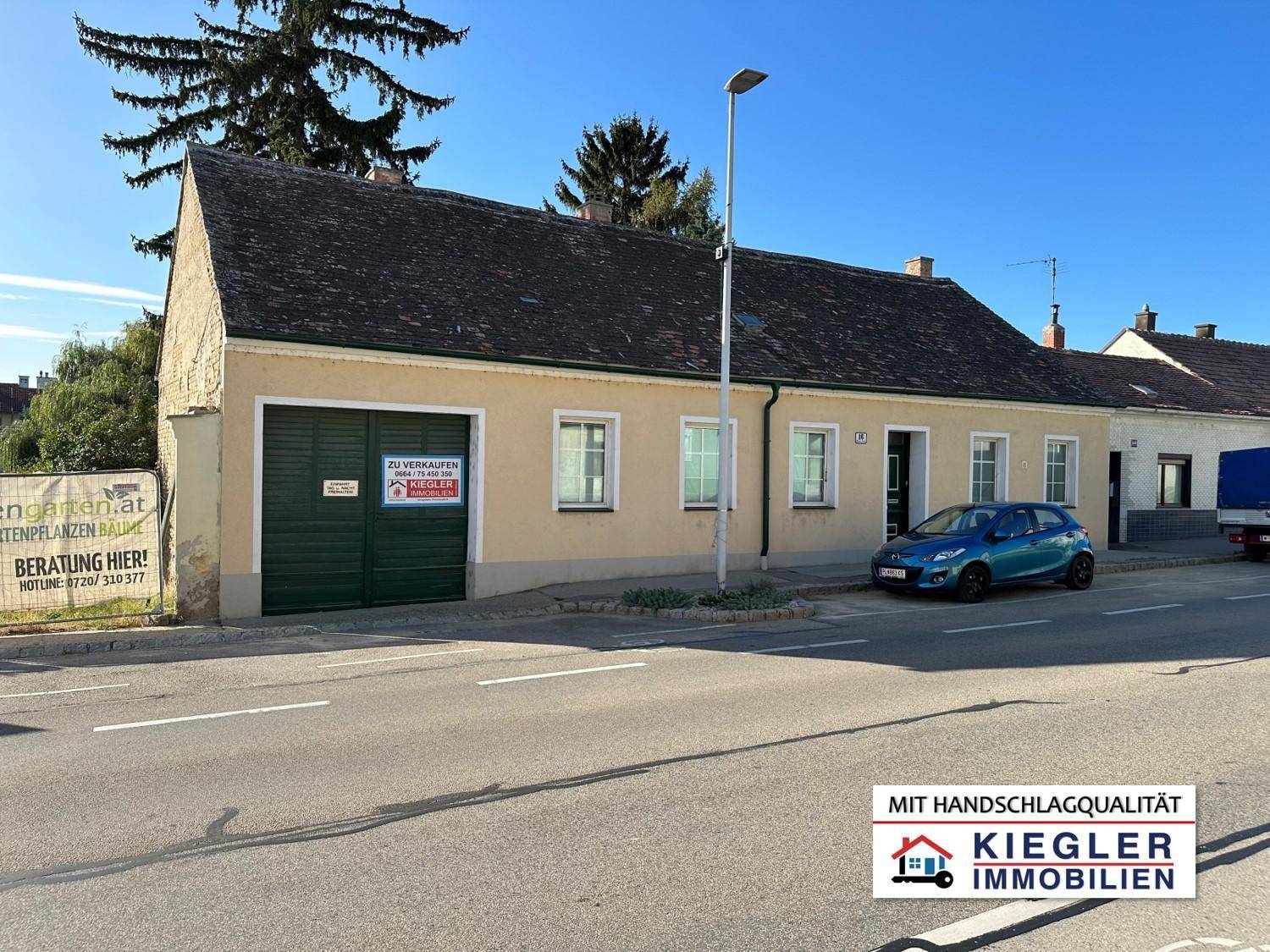 Einfaches Wohnhaus mit beiger Fassade und Satteldach direkt an der Straße gelegen.