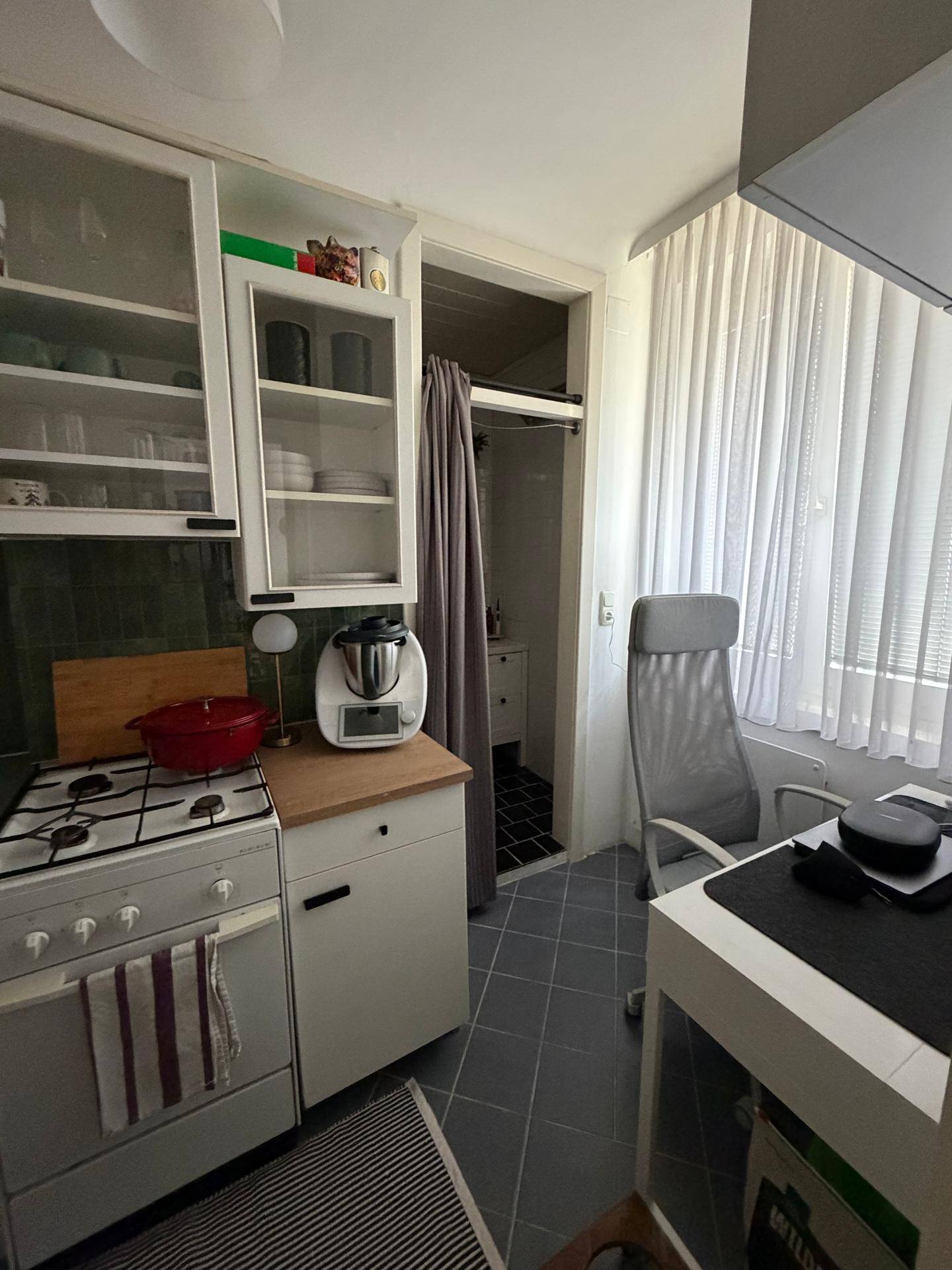 Küchenbereich mit Herd und Schränken, angrenzend an einen Arbeitsplatz mit Blick auf ein Badezimmer.