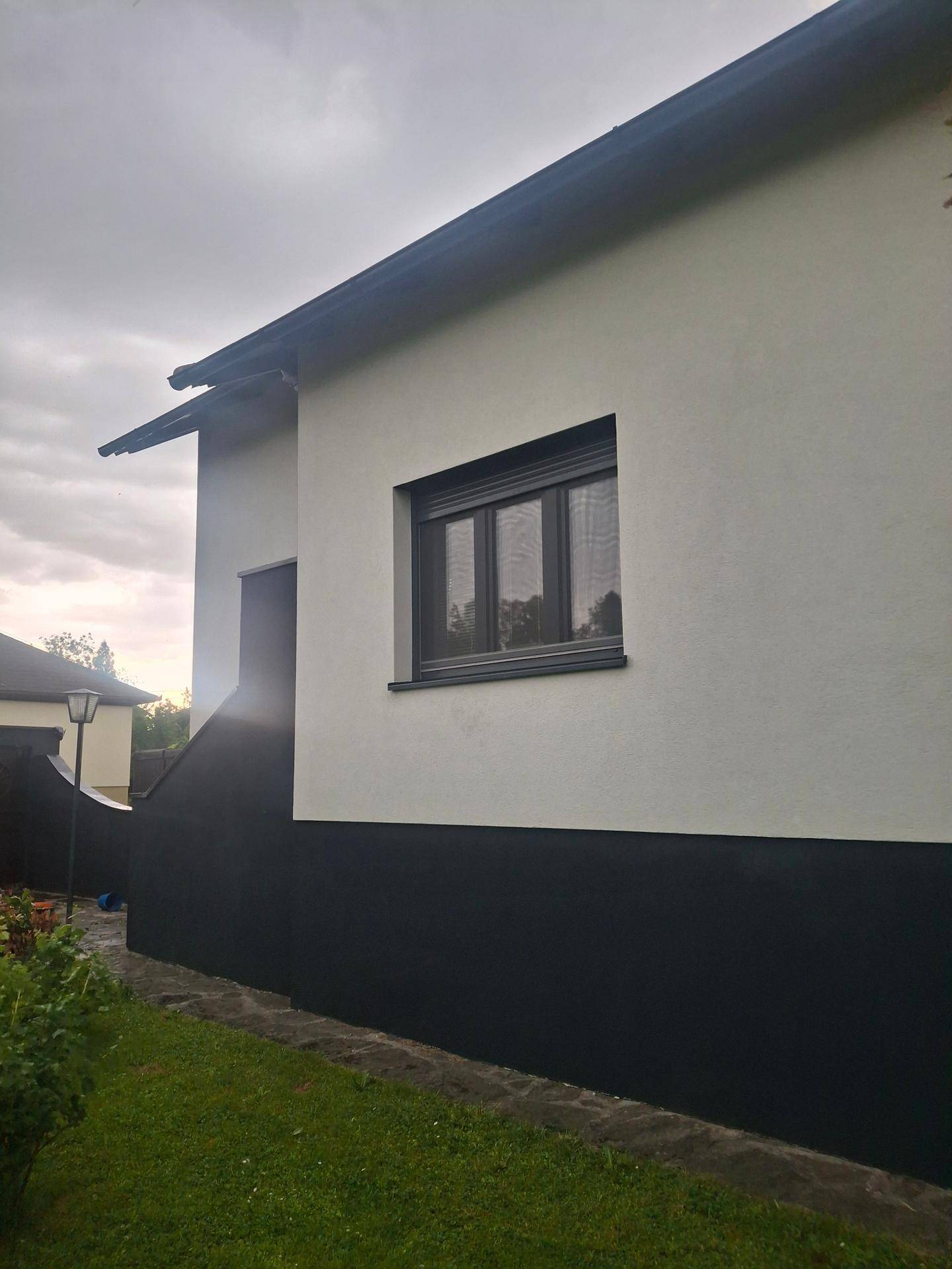 Seitenansicht des Hauses mit weißer Fassade und dunklem Sockel.