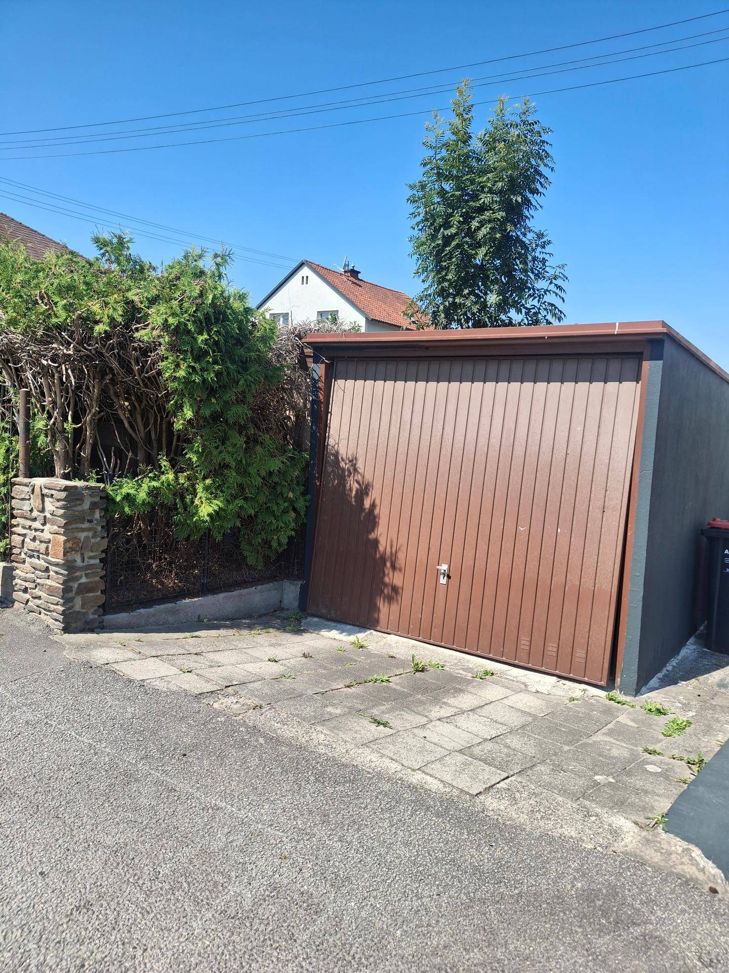 Einzelgarage mit braunem Tor und umgebender Hecke.