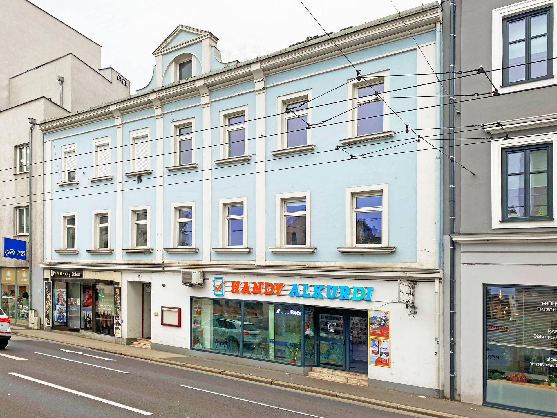 Historische Fassade eines hellblauen Gebäudes mit Geschäften im Erdgeschoss.