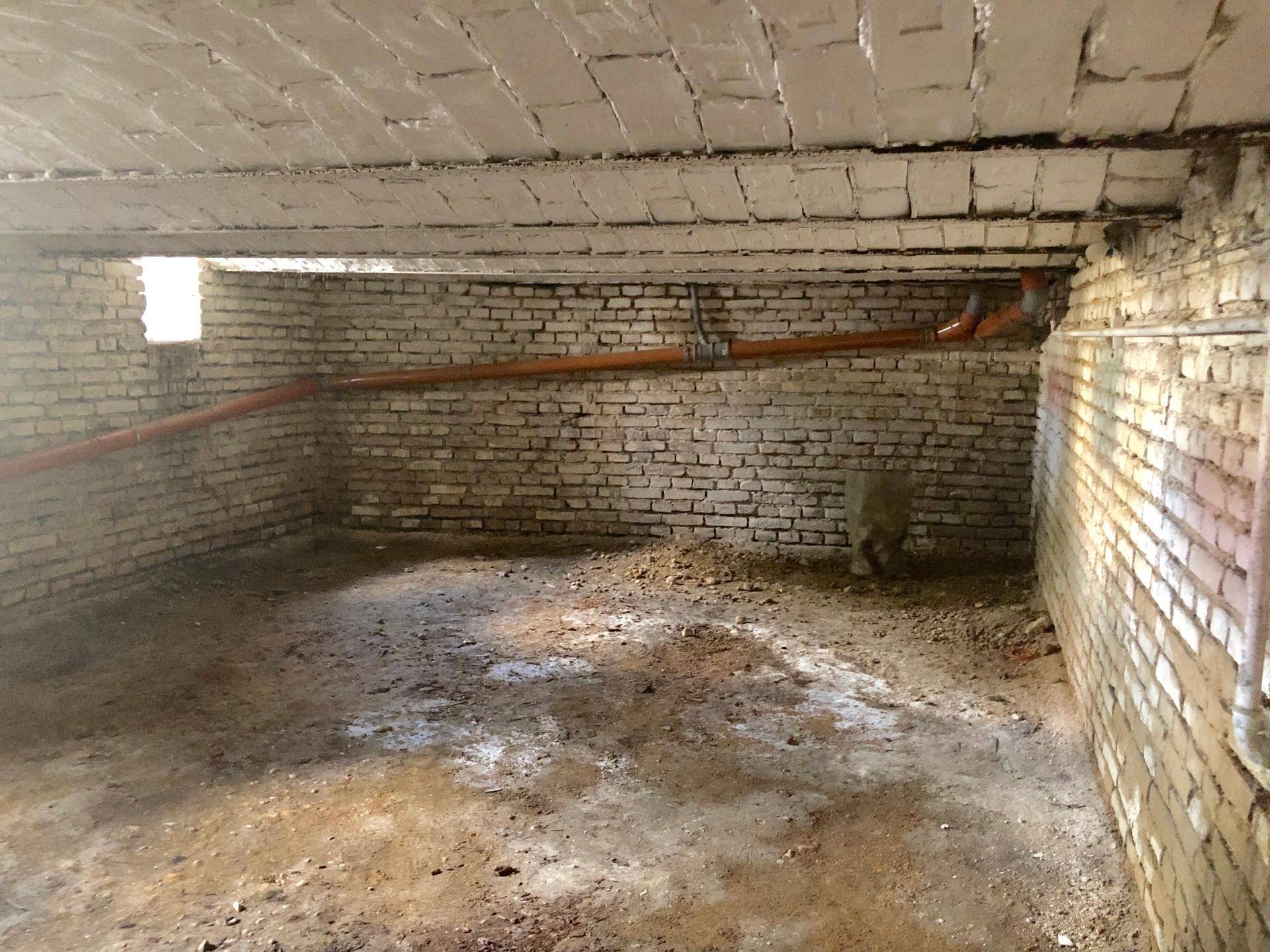 Unfertiger Kellerraum mit unverputzten Ziegelwänden und sichtbaren Rohren.