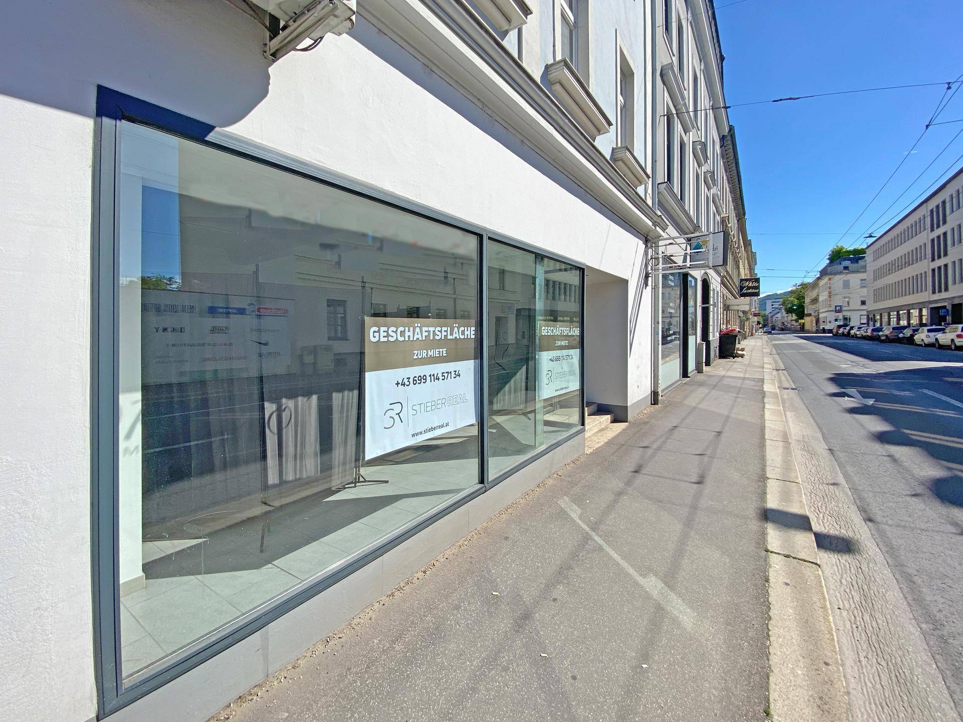 Außenansicht der Geschäftsfläche an einer belebten Straße mit großen Schaufenstern und Mietanzeige.