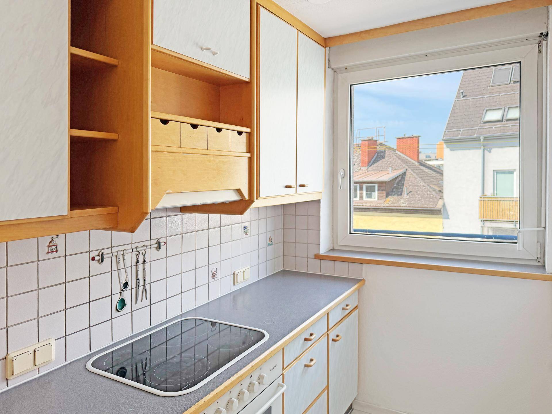 Küchenzeile mit Induktionskochfeld, gefliestem Spritzschutz und Fenster mit Blick nach draußen.