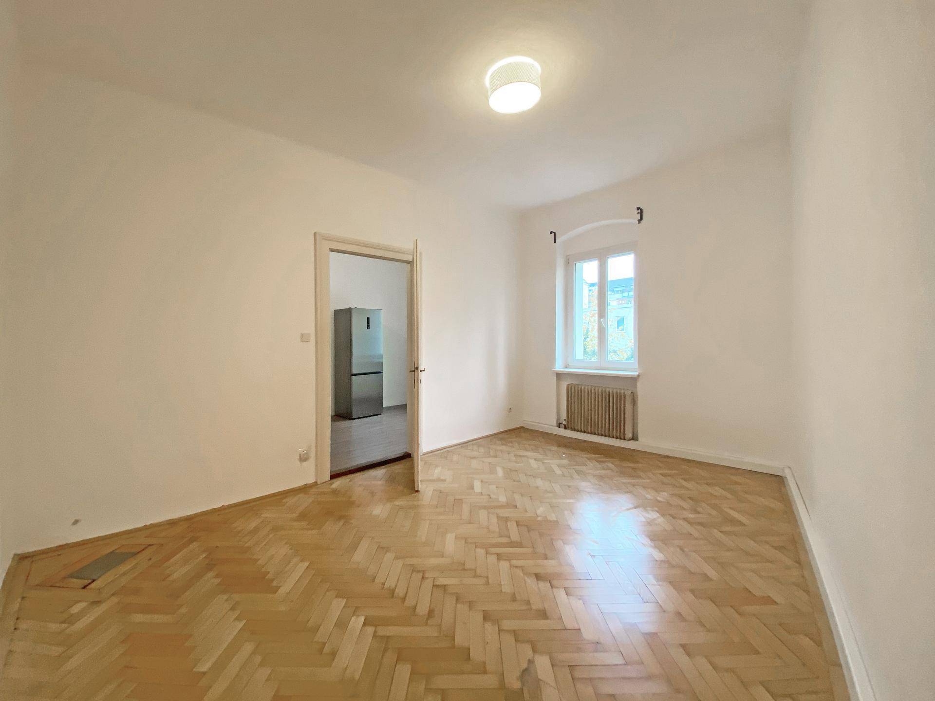 Leeres Zimmer mit Fischgrätparkettboden und Fenster, mit Blick auf einen angrenzenden Raum.