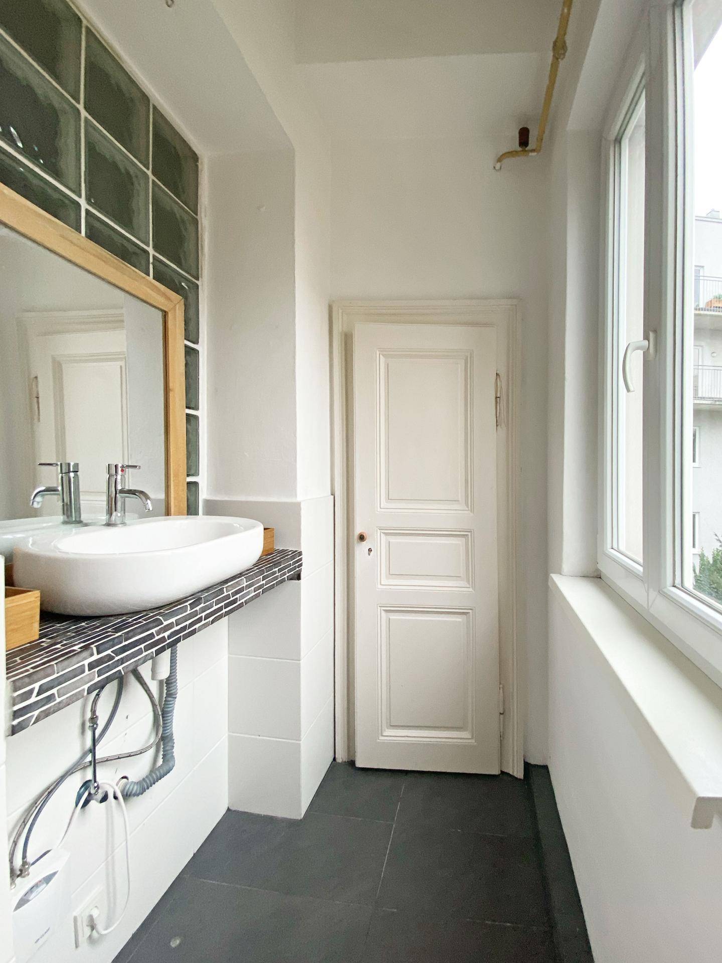 Helles Badezimmer mit modernem Waschbecken, Mosaikfliesen und großem Fenster.