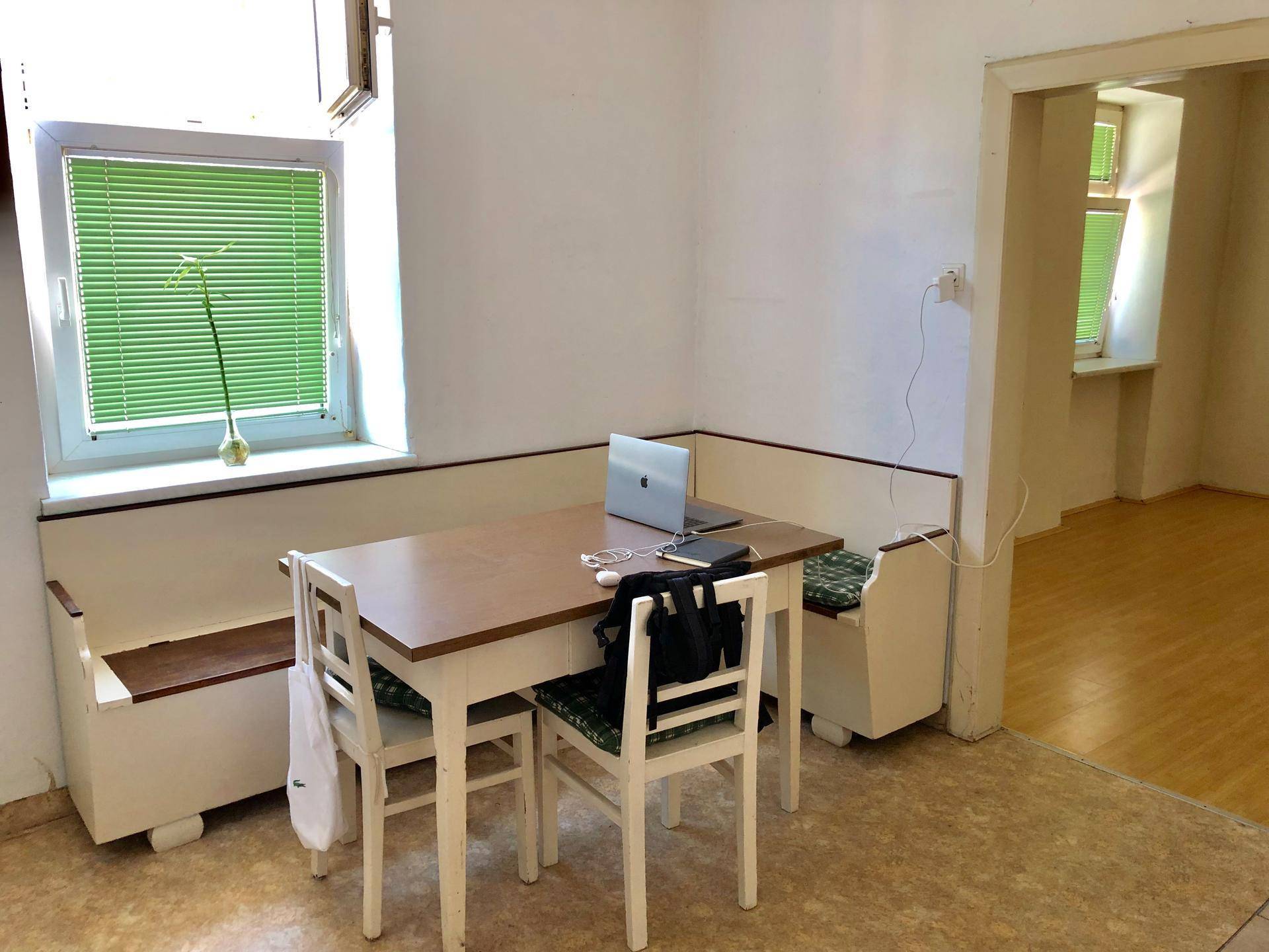 Einfacher Essbereich mit Holztisch, Sitzbank und Blick auf einen weiteren Raum.