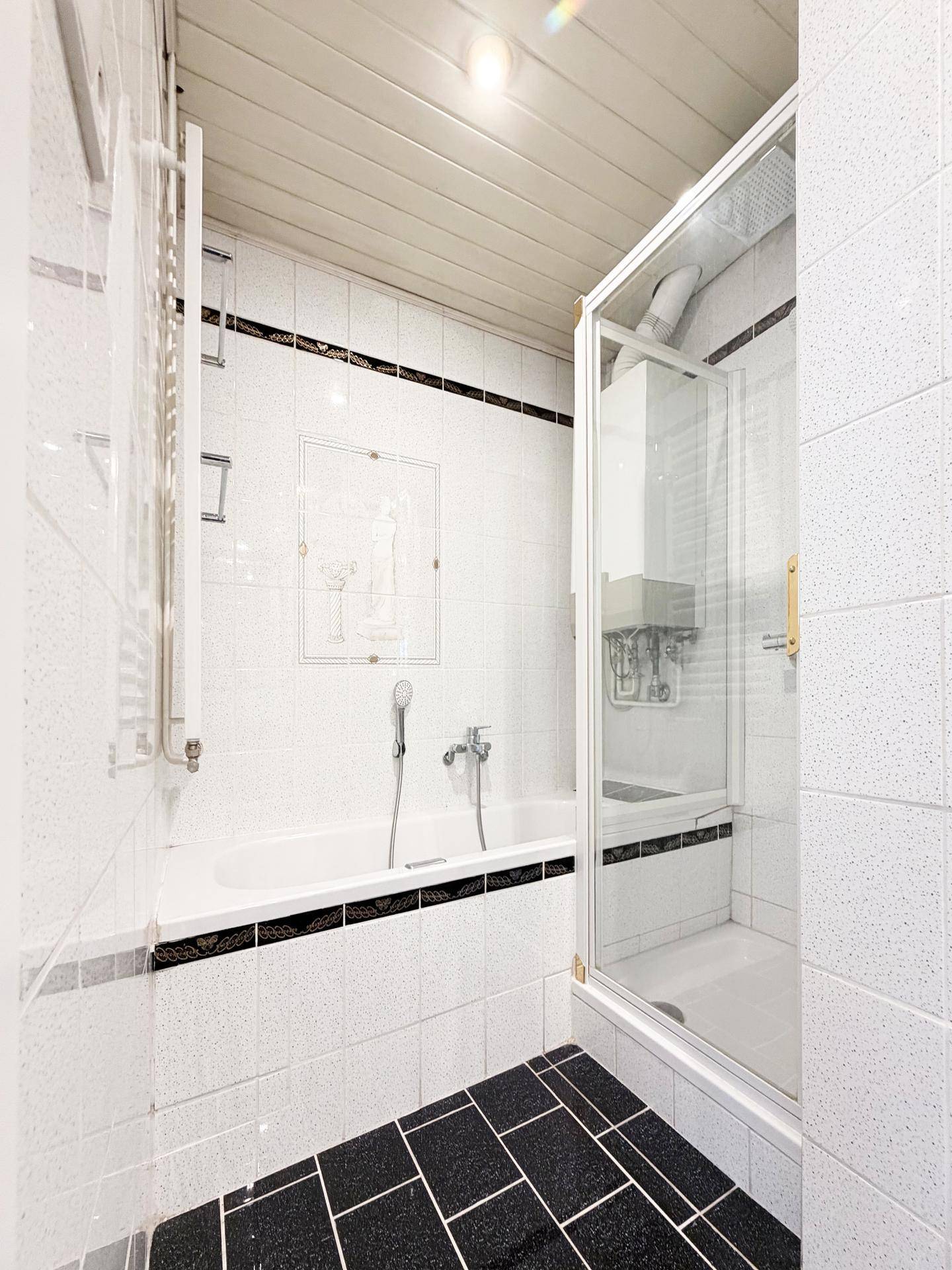 Badezimmer mit Badewanne, Duschkabine, schwarz-weißen Fliesen und Holzdecke.