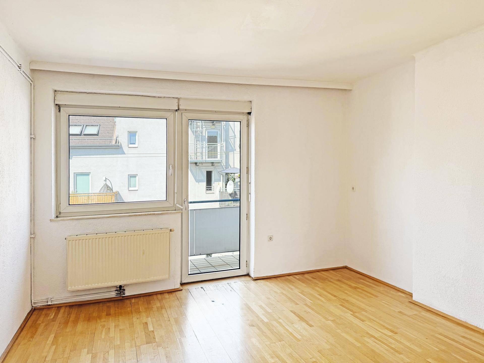 Heller Raum mit Holzboden und Zugang zu einem kleinen Balkon oder einer Loggia.