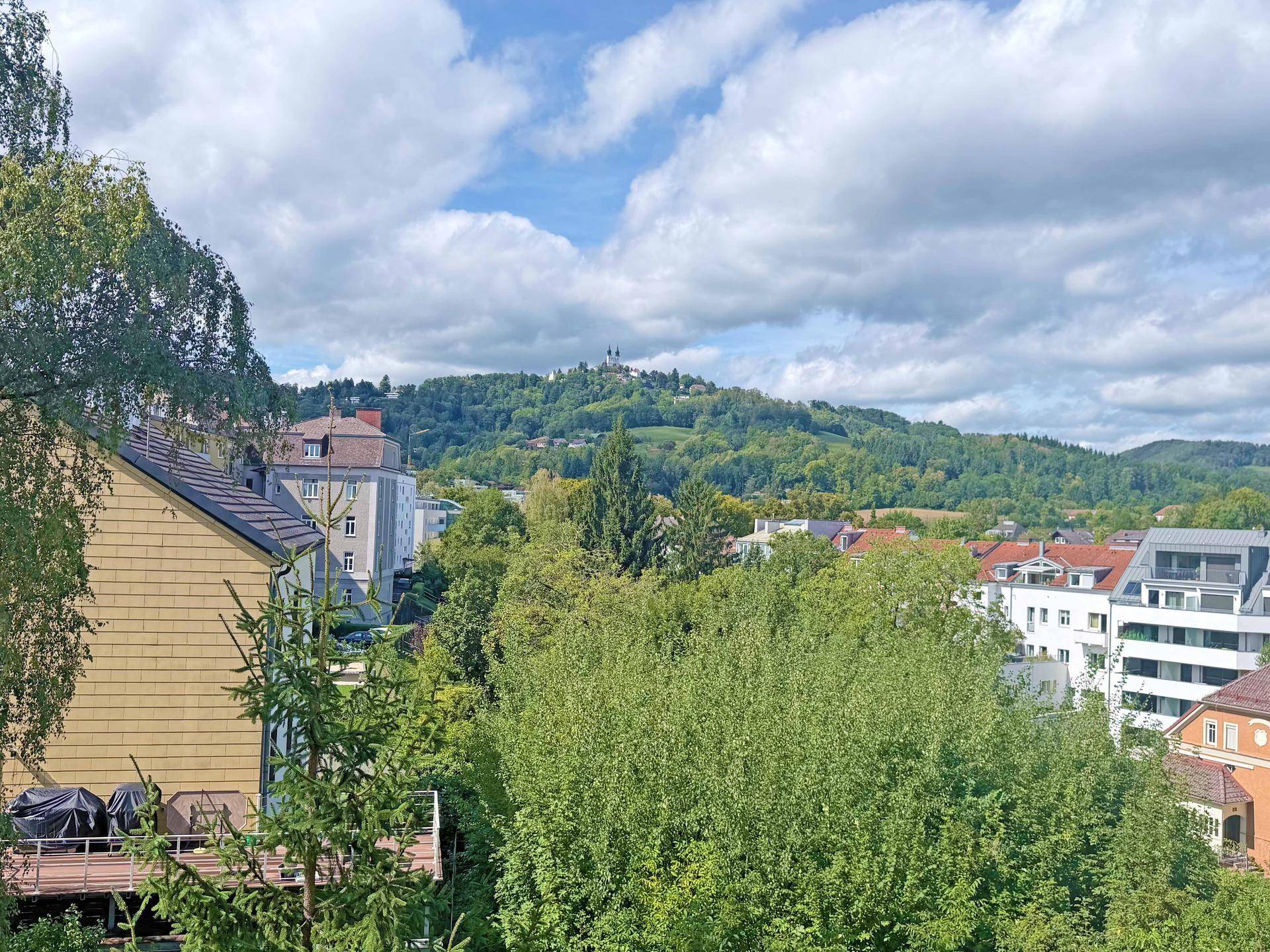 Weitläufiger Blick über grüne Hügel und die Stadt mit historischer Bebauung.