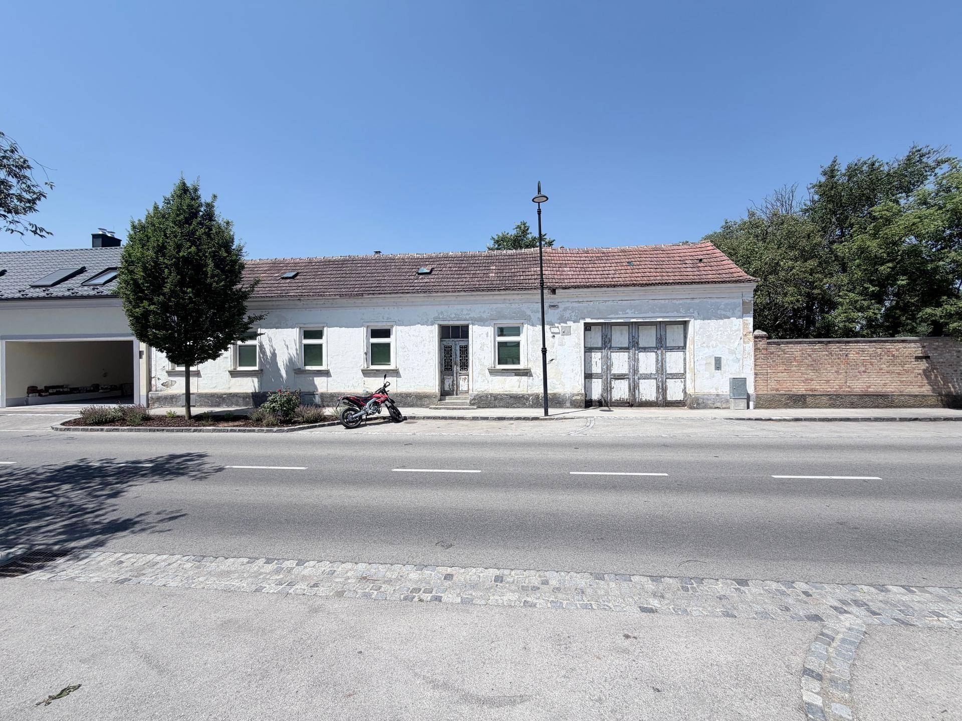 Sonnige Straßenansicht des Anwesens mit weißer Fassade und einem Motorrad davor.