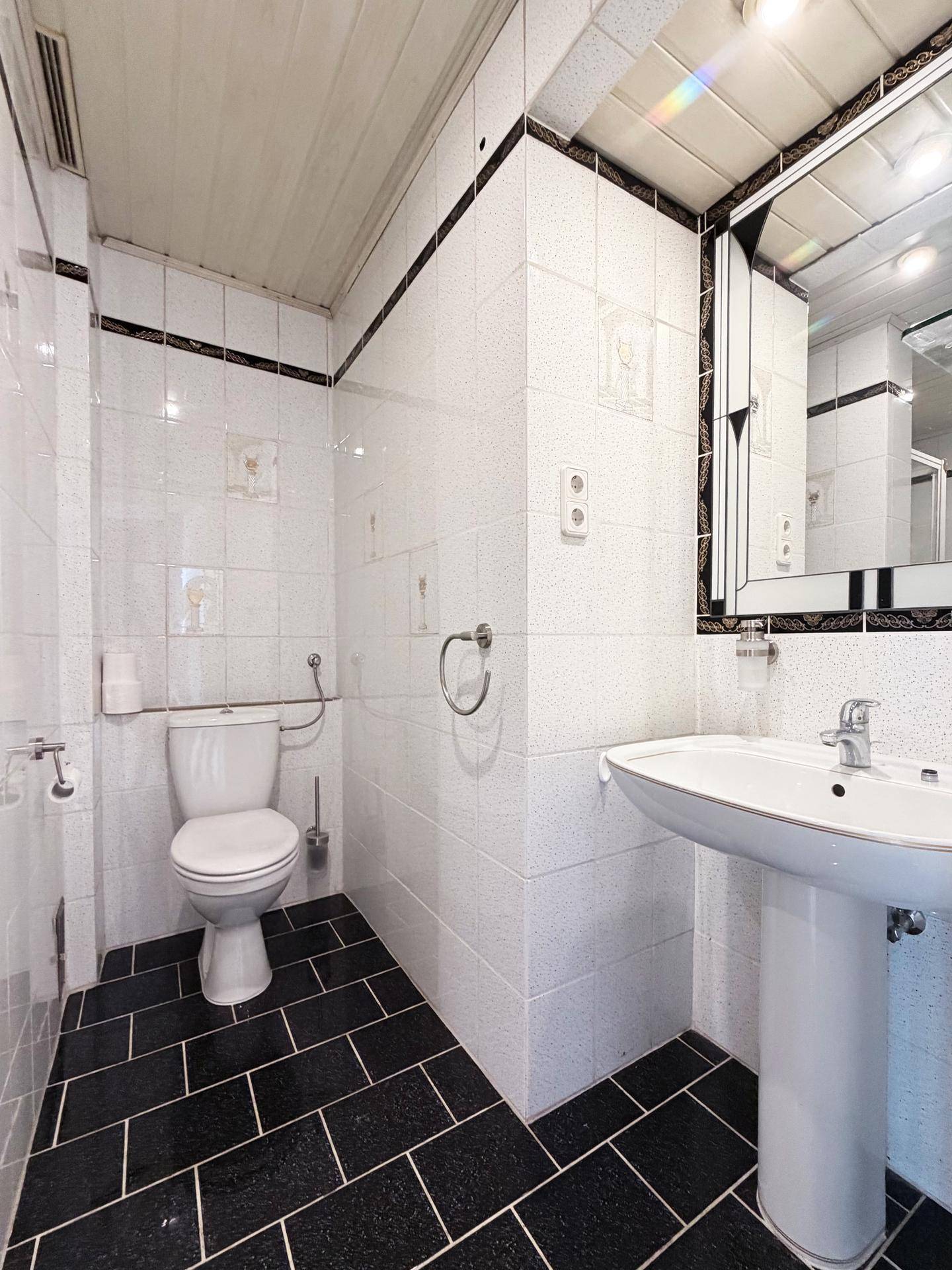 Badezimmer mit Toilette, Waschbecken, Spiegelschrank und schwarz-weißen Fliesen.
