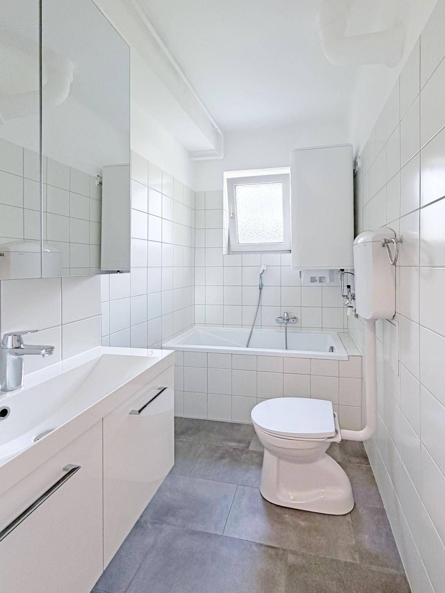 Modernes Badezimmer mit Badewanne, WC, Waschtisch und Fenster für Tageslicht.