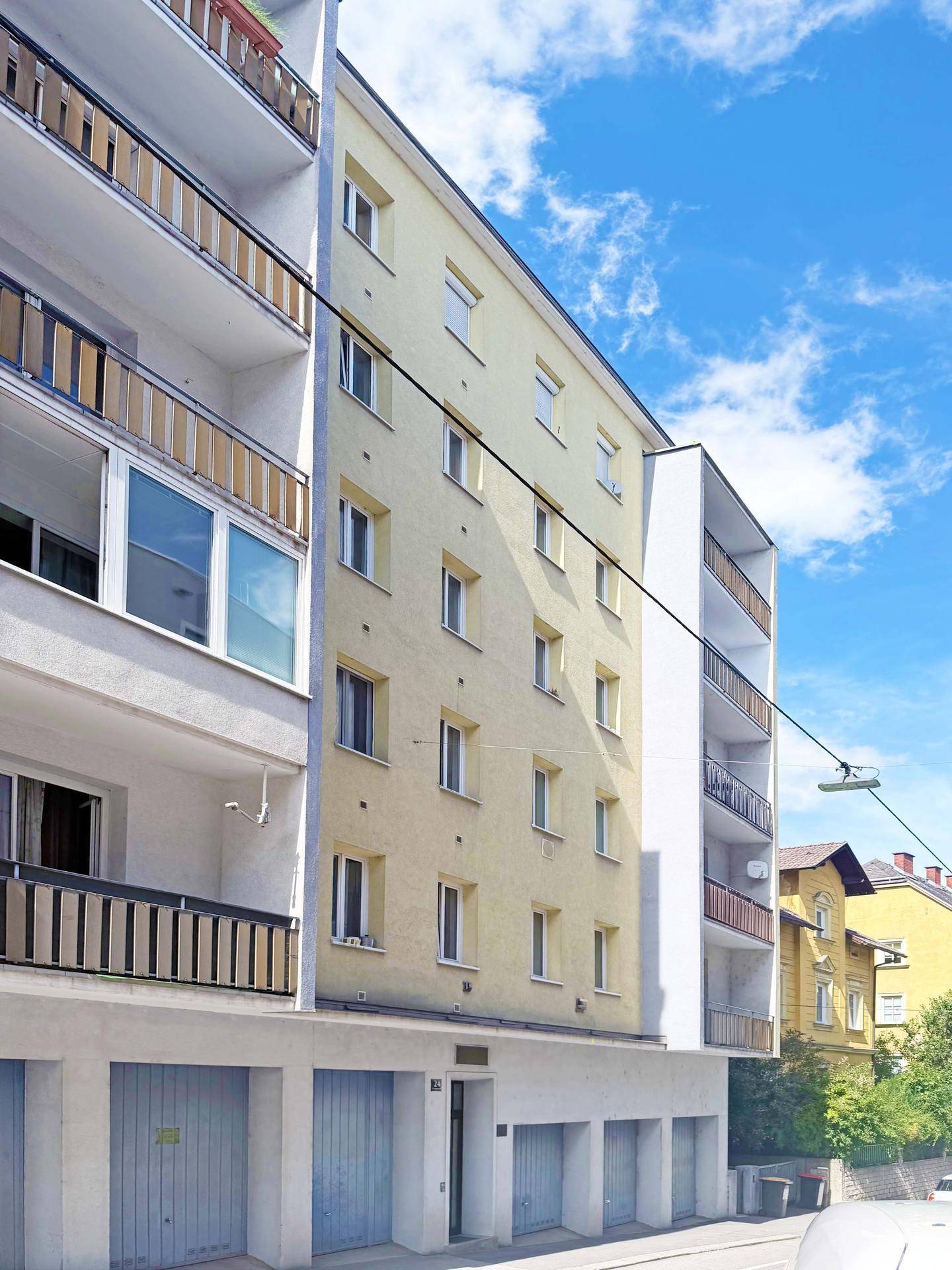 Mehrstöckiges Wohngebäude mit gelber Fassade, Balkonen und Garagen im Erdgeschoss.