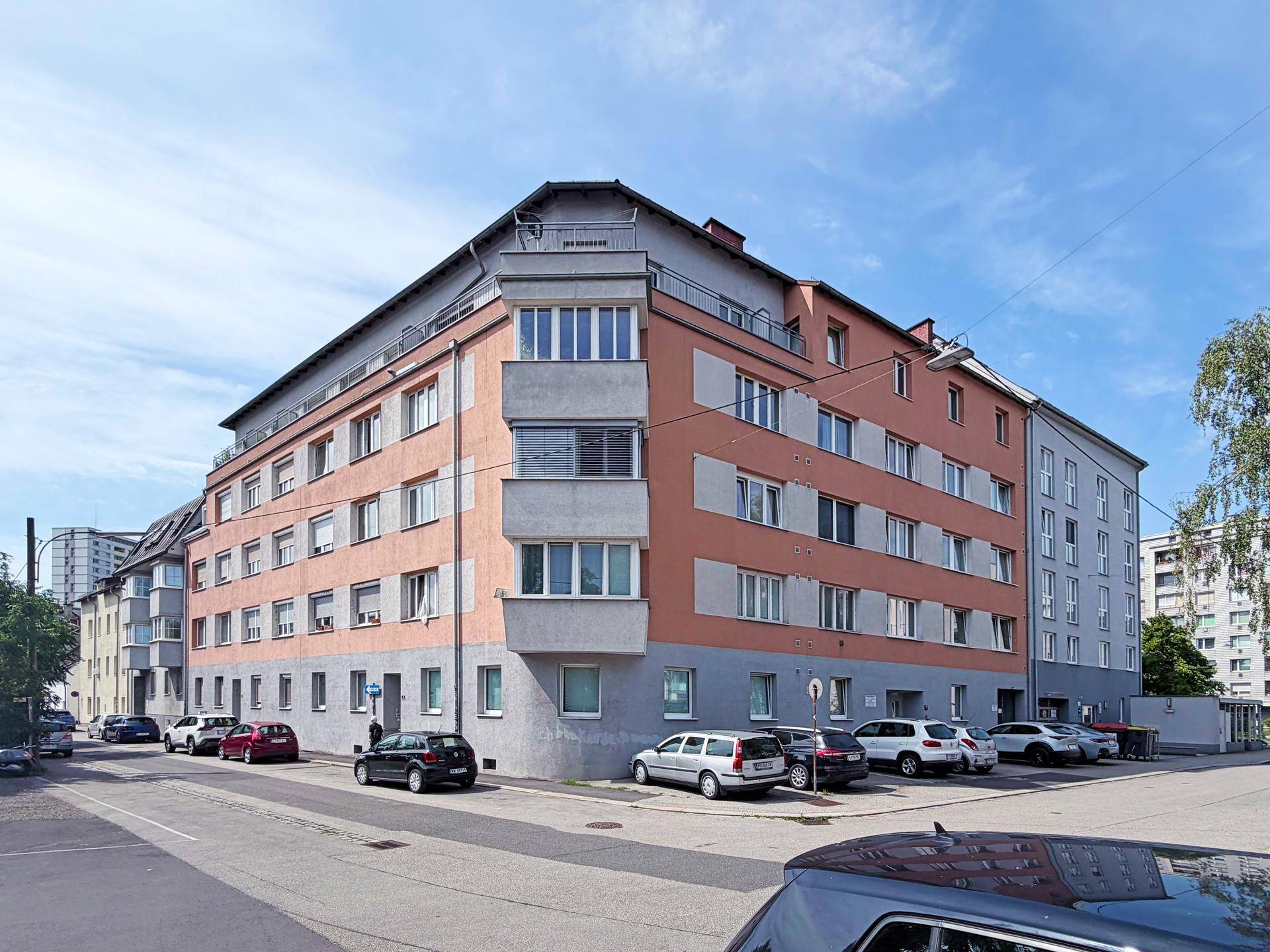 Großes Apartmentgebäude mit markanter Fassade und geparkten Autos an der Straße.