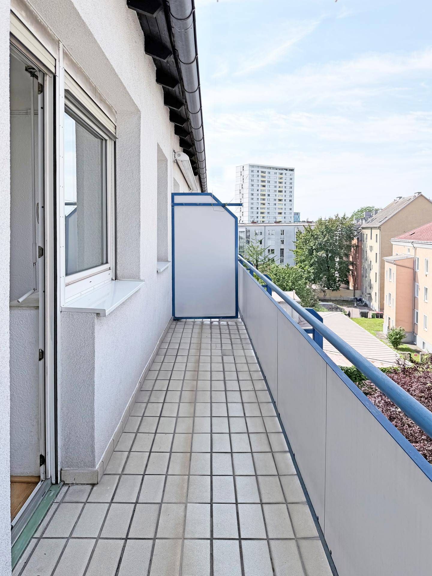 Langer, schmaler Balkon mit Fliesenboden und blauen Geländern, bietet Blick auf die Stadt.