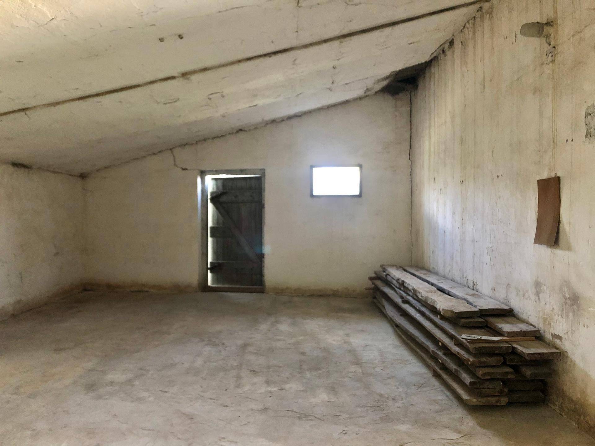 Einfacher Dachbodenraum mit schräger Decke, Holztür und gestapelten Holzbrettern.