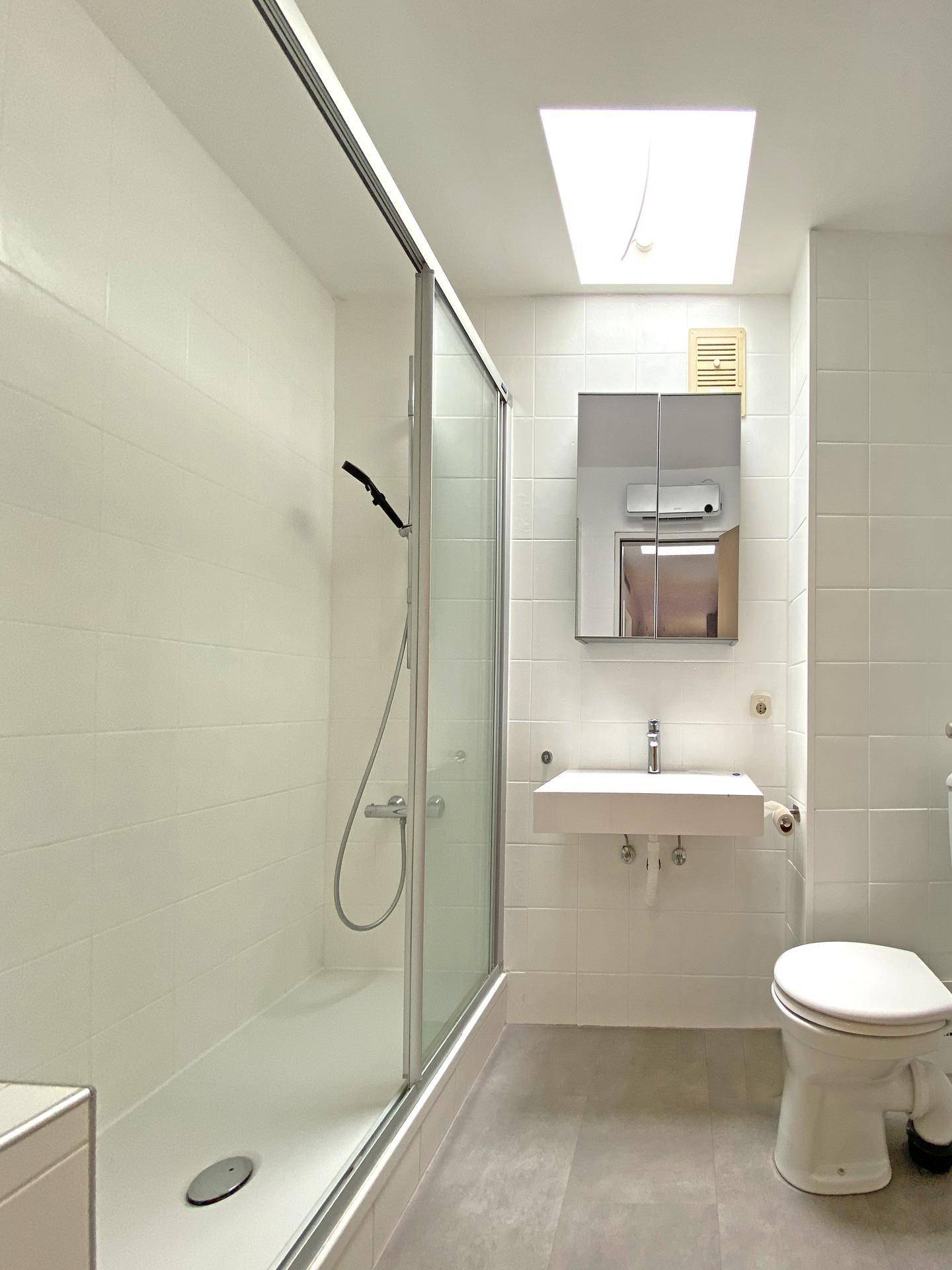 Modernes Badezimmer mit ebenerdiger Dusche, wandhängendem Waschbecken und einem Oberlicht für Tageslicht.