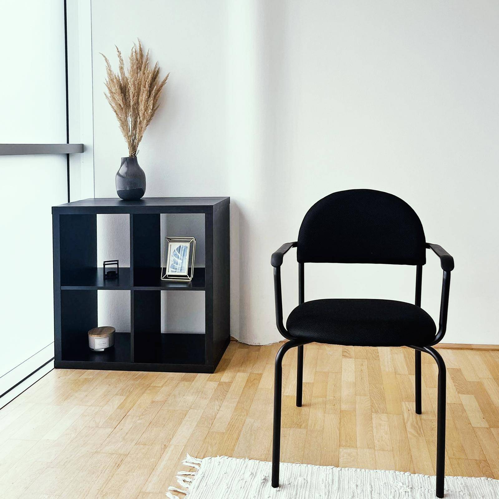 Minimalistischer Bereich mit schwarzem Stuhl, kleinem schwarzen Regal und Holzboden neben einem großen Fenster.