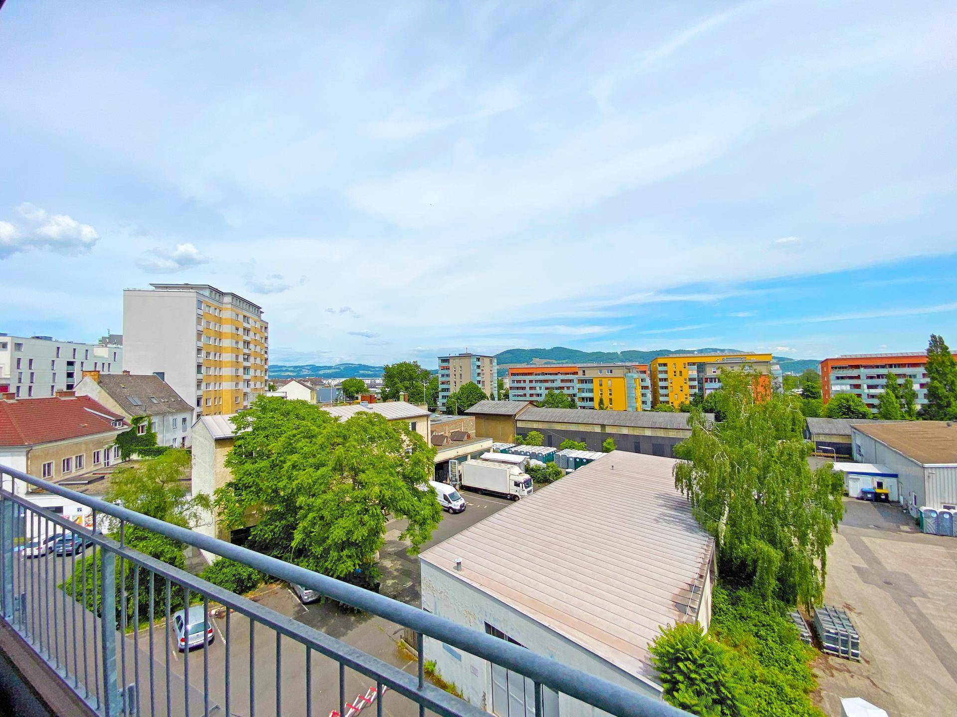 Panoramablick über eine städtische Landschaft mit Gebäuden, Bäumen und fernen Hügeln.