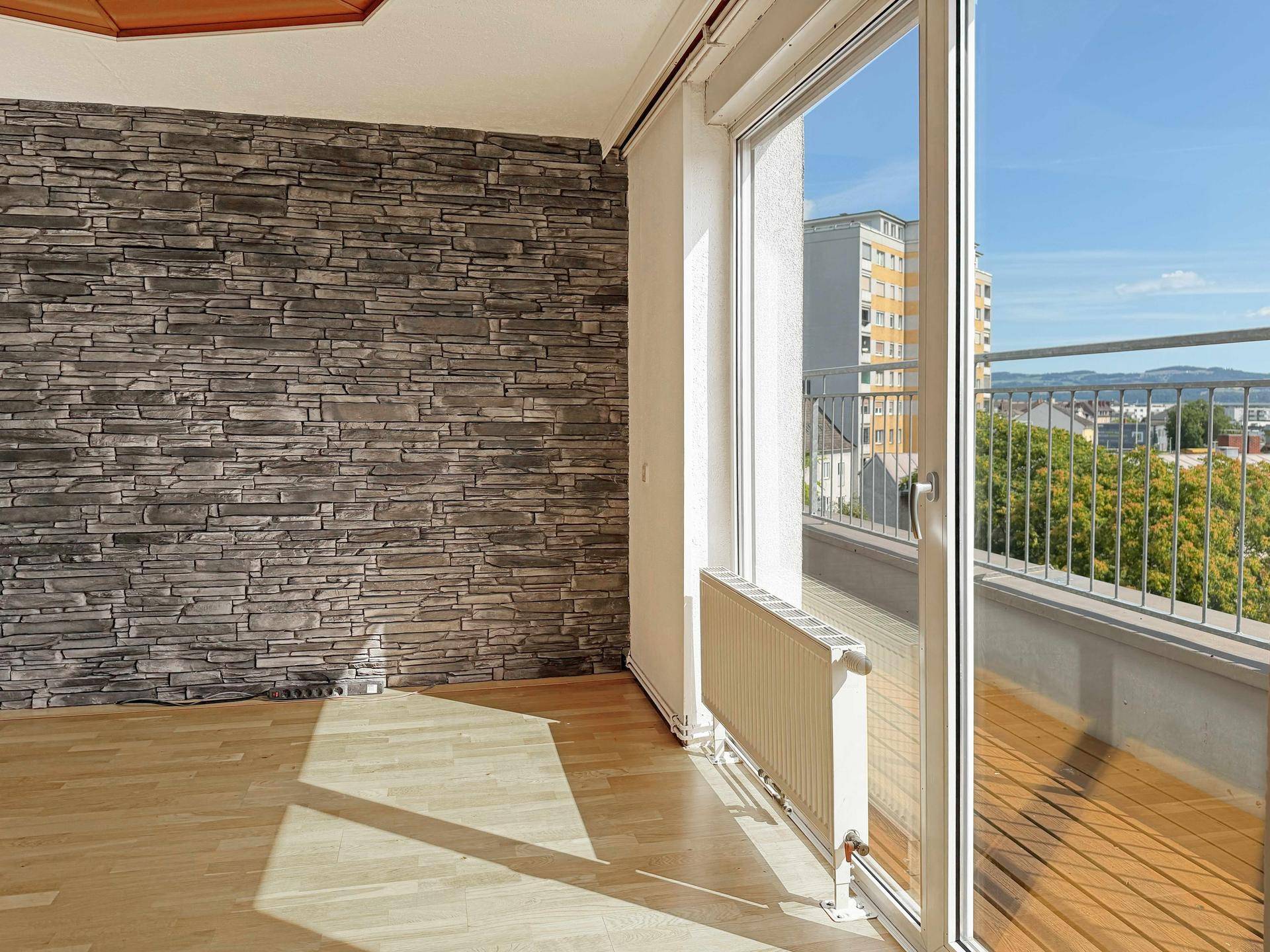 Heller Raum mit Steinwand-Akzent, Holzboden und Zugang zu einem Balkon mit Weitblick.