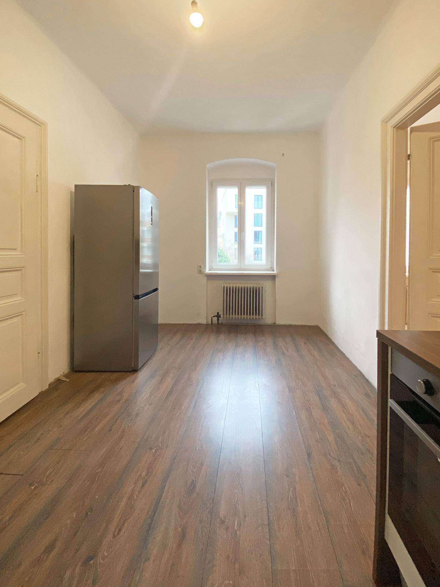 Heller Küchenbereich mit Holzboden, Fenster und einem modernen Kühlschrank.