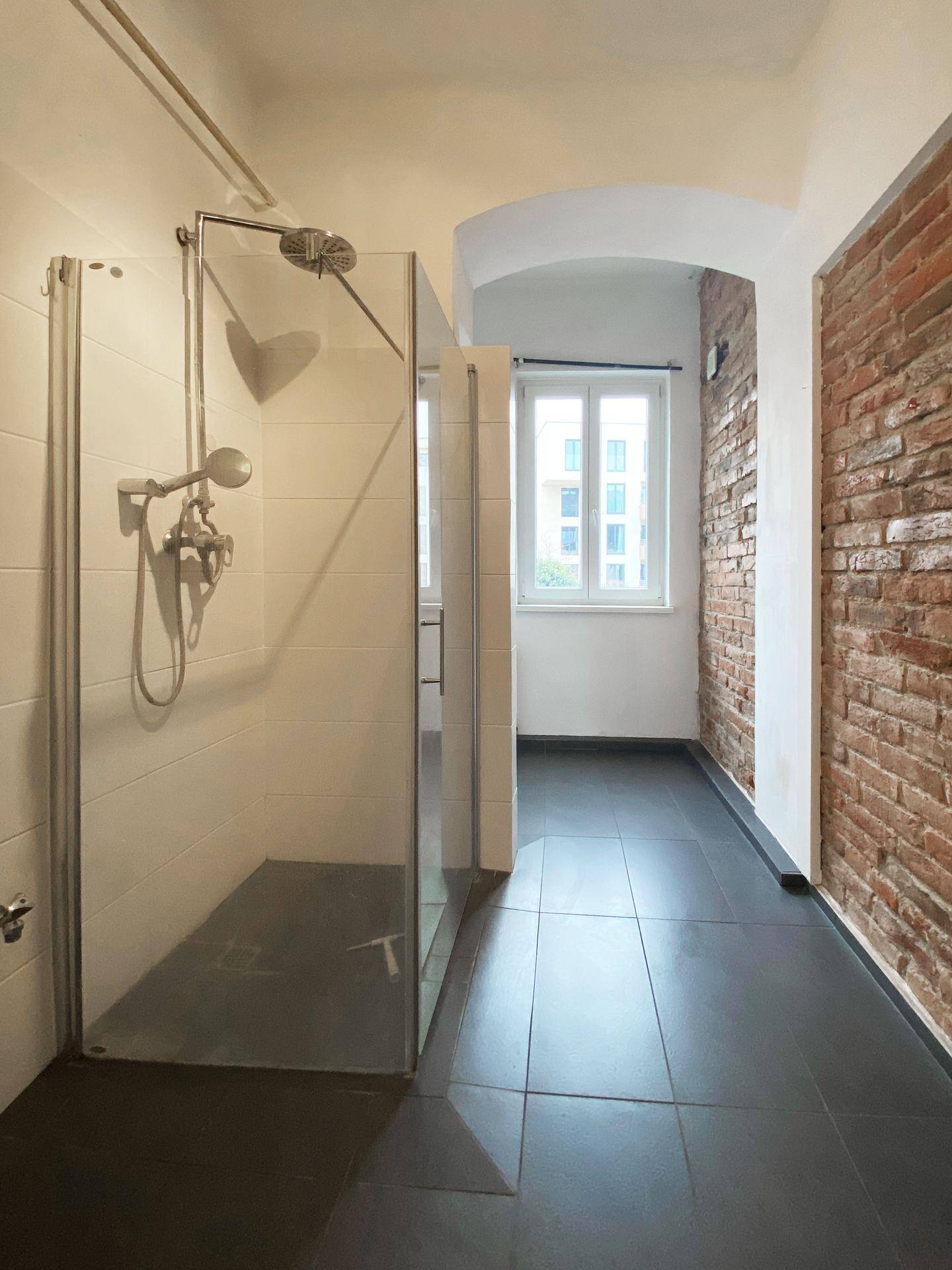 Modernes Badezimmer mit dunklen Fliesen, Glasdusche und einer charakteristischen Ziegelwand.