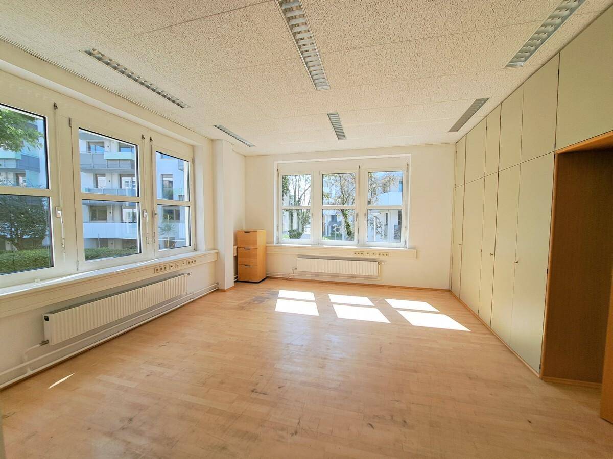 Geräumiges Büro mit Laminatboden, Einbauschränken und großen Fenstern, die viel Licht hereinlassen.