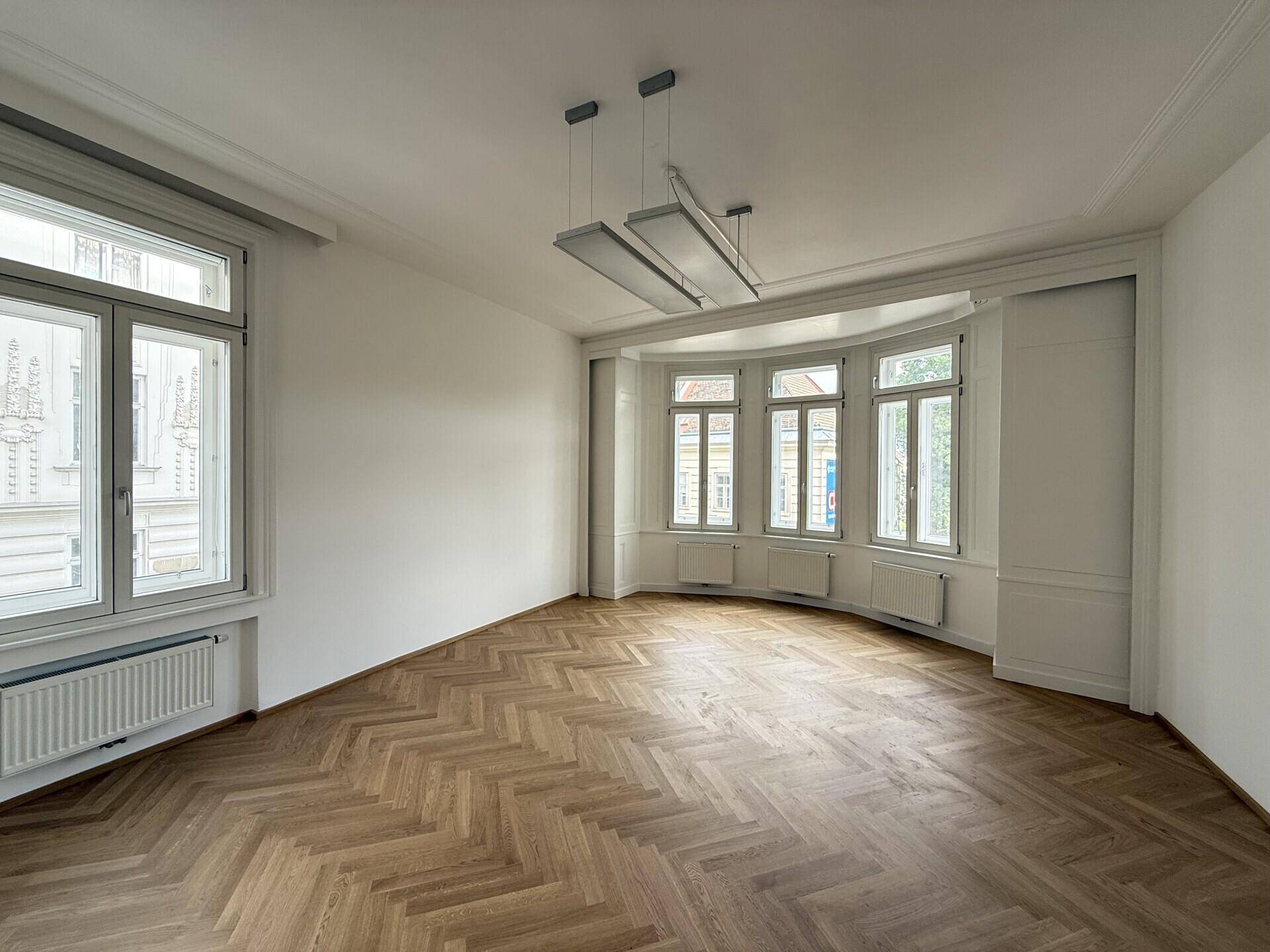 Büro mit Fischgrätparkett, großen Fenstern und einem Erker, der viel Licht hereinlässt und Stadtblick bietet.