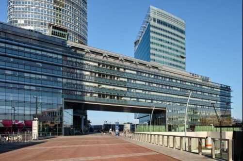 Moderne Architektur mit Glasfassaden und einer markanten Brückenkonstruktion, die zwei Gebäudeteile verbindet.