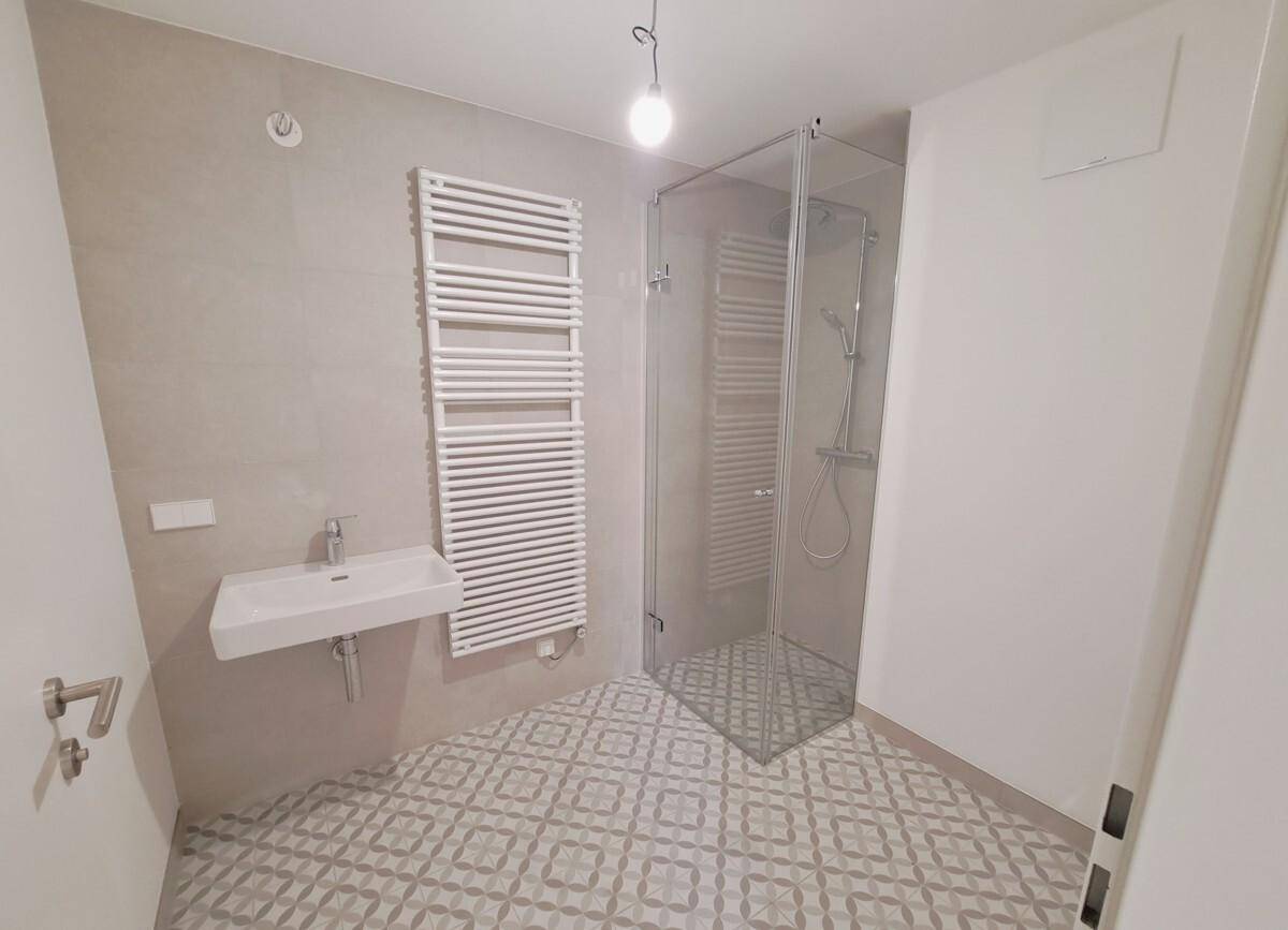 Modernes Badezimmer mit Duschkabine, Handtuchheizkörper und stilvollen Fliesen am Boden und an der Wand.