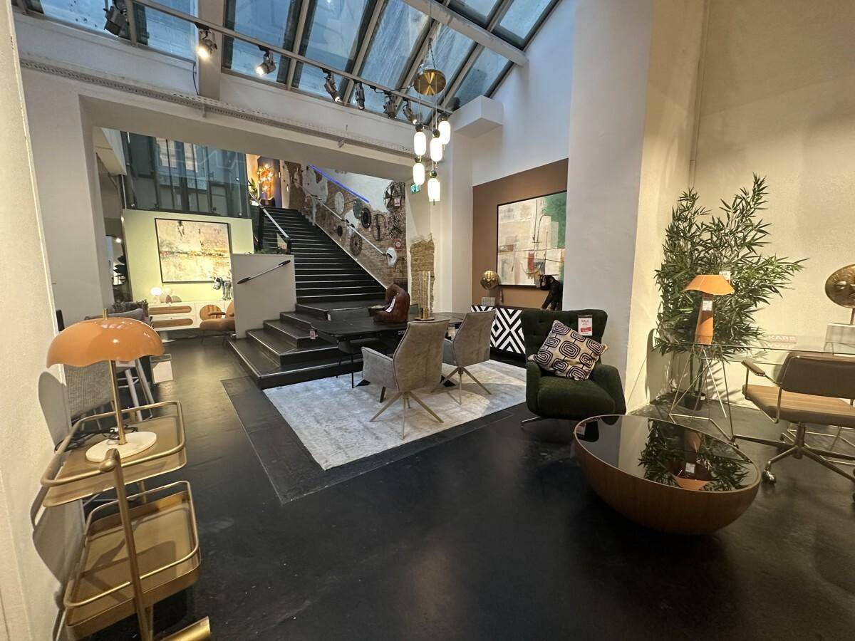 Offener Verkaufsbereich mit einer zentralen Treppe, Glasdach und vielfältigen Möbeln.