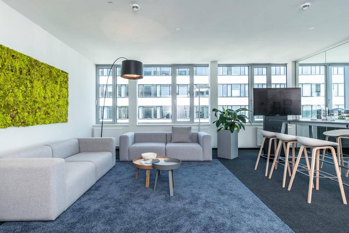Gemütlicher Loungebereich mit bequemen Sofas, Teppichboden und einer Mooswand als Dekoration.