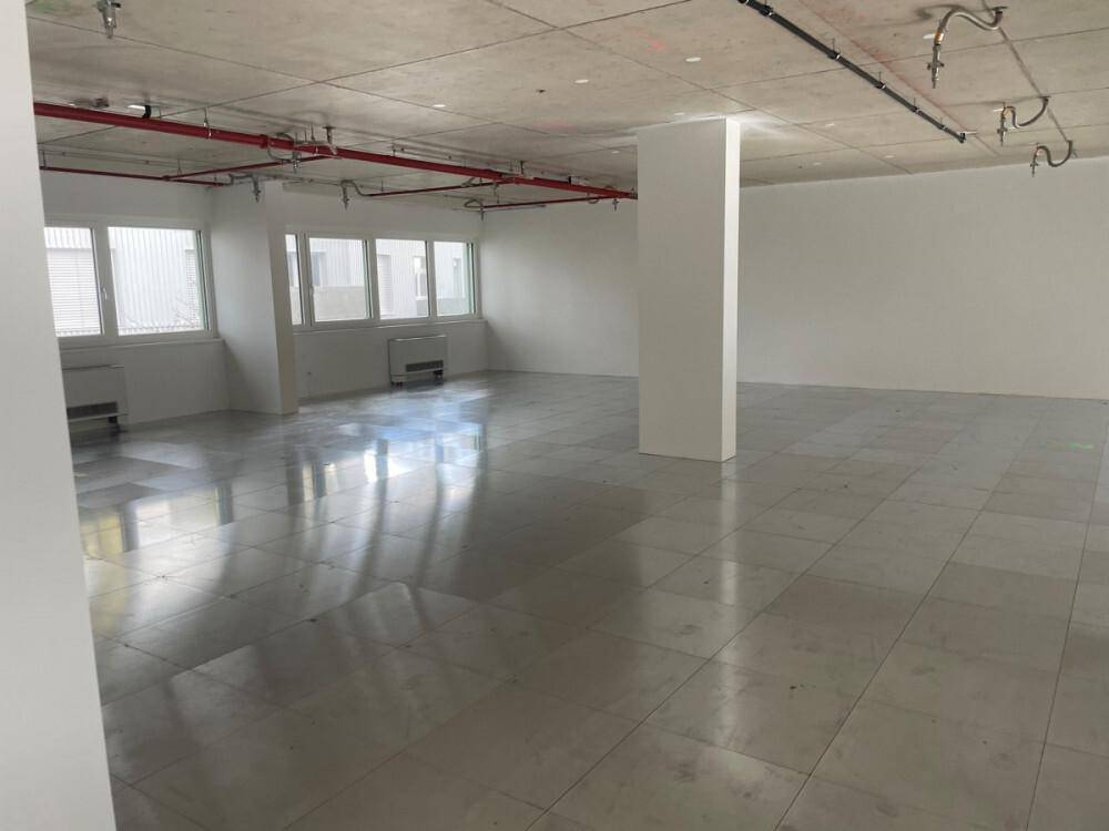 Offener Gewerberaum mit Beton-Decke, Fliesenboden und tragenden Säulen, bereit für den Innenausbau.