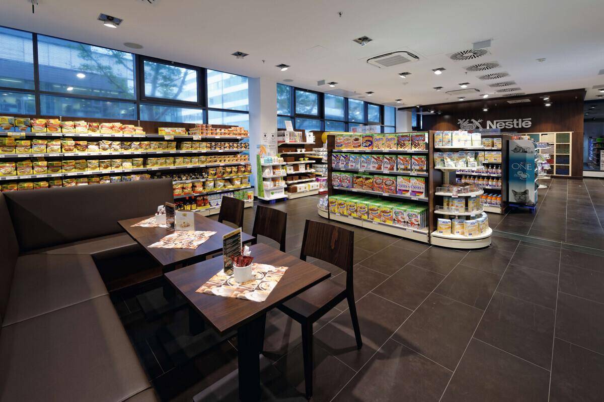 Gut sortierter Supermarkt mit breiten Gängen, Regalen voller Produkte und einem kleinen Café-Bereich.