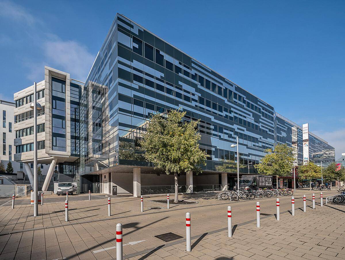 Weitläufige Ansicht des modernen Bürokomplexes mit markanter Glasfassade und Fahrradständern im Vordergrund unter blauem Himmel.